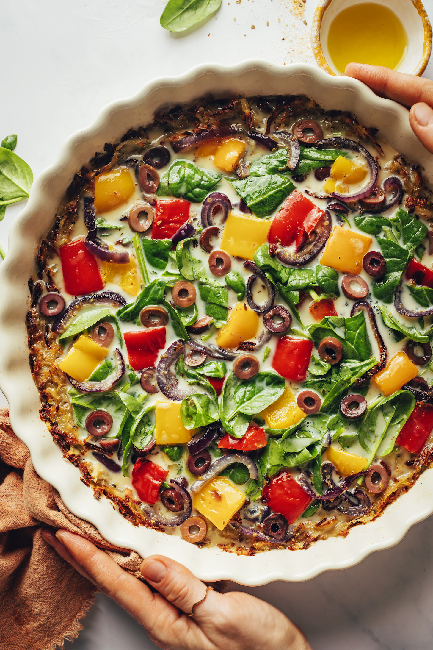 Hands hold a dish of unbaked mediterranean quiche