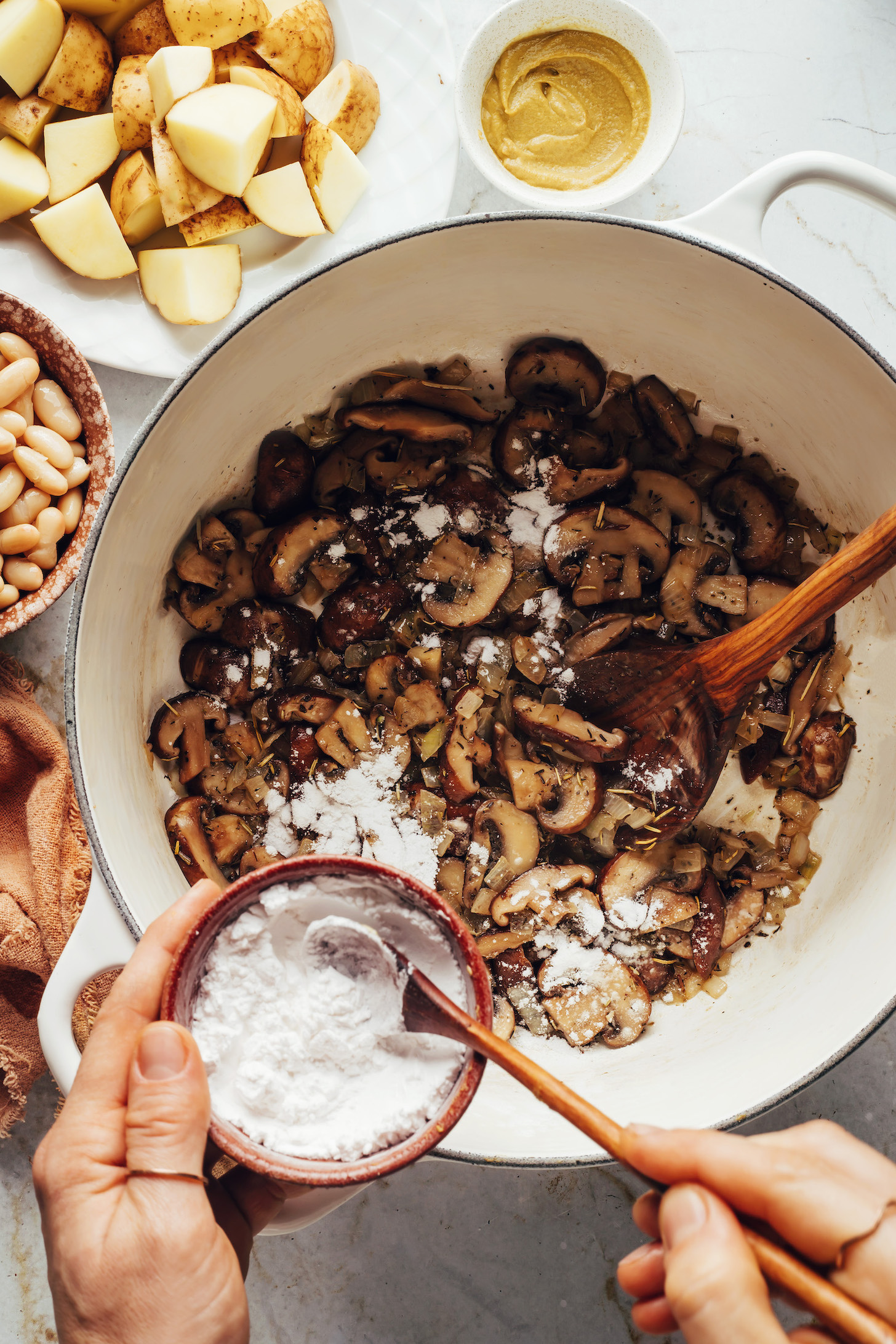 Adding cornstarch to a pot of sautéed mushrooms and herbs