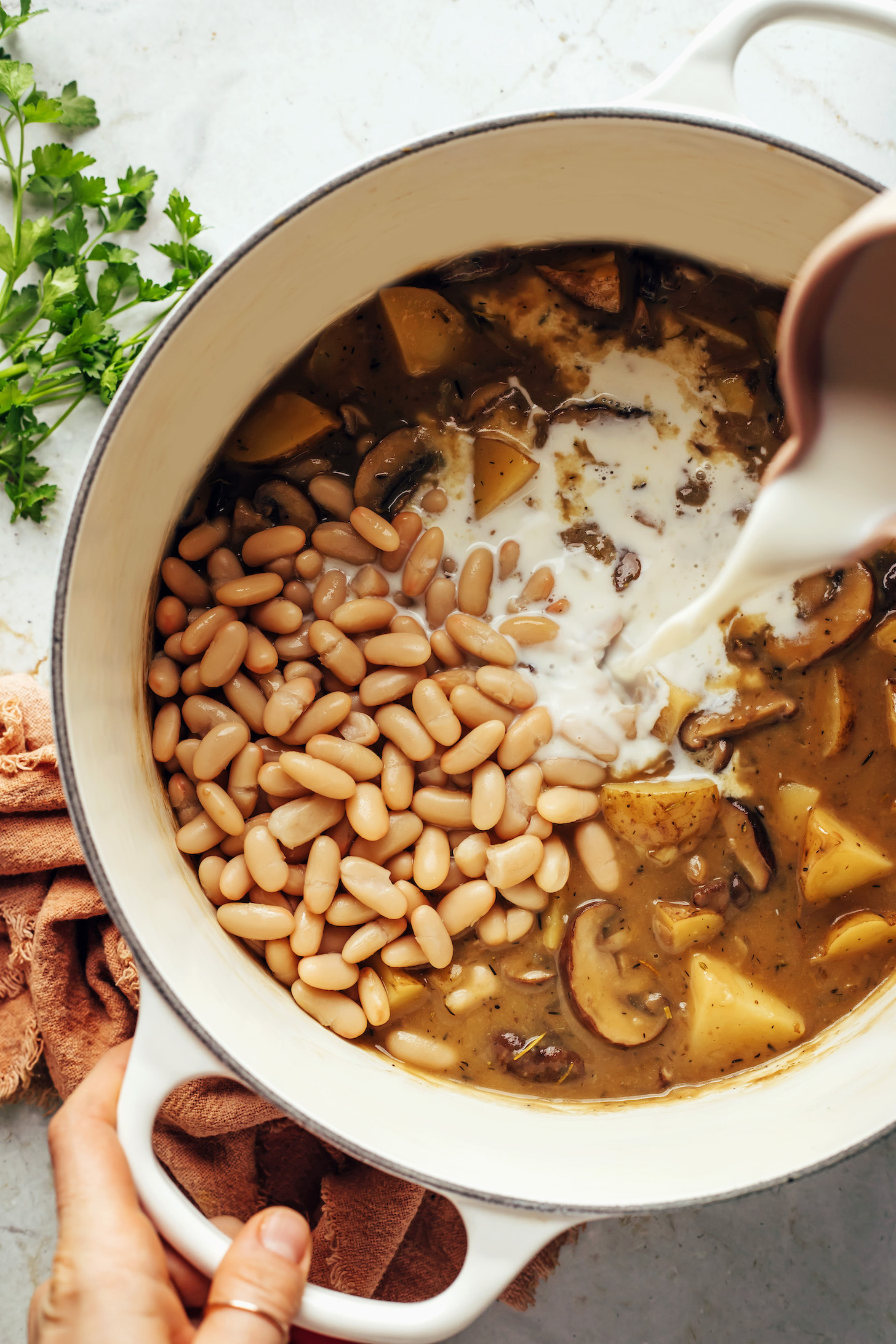 Pouring almond milk into a pot of white bean mushroom stew