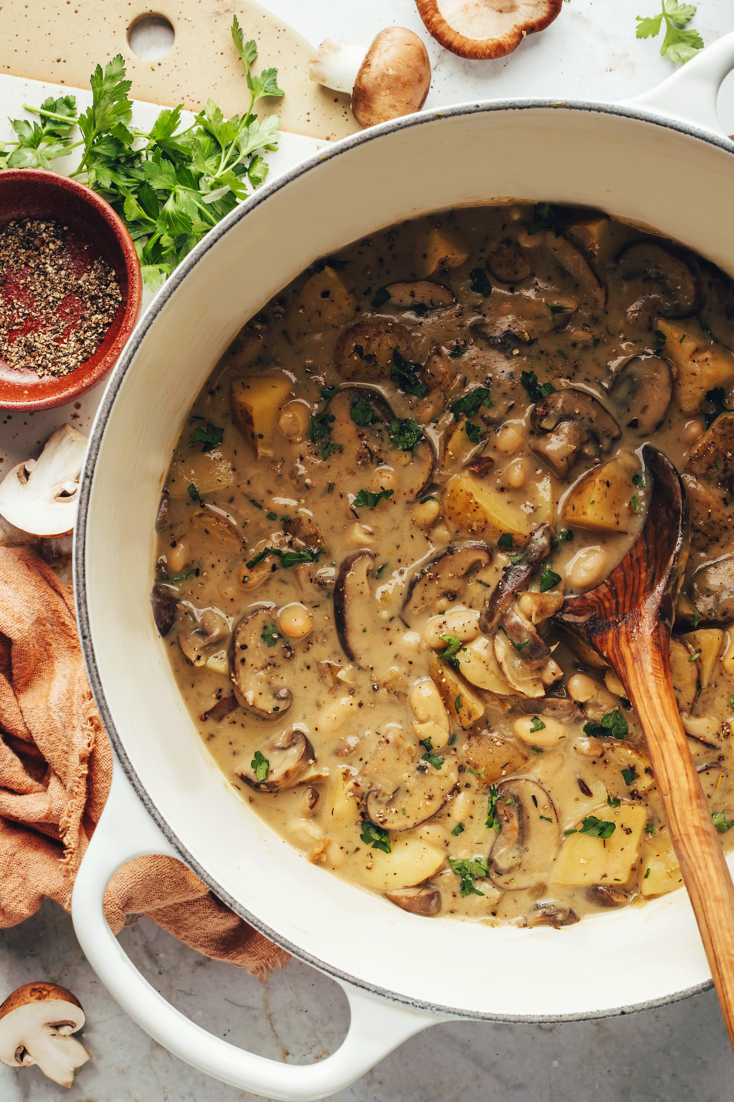 Parsley, mushrooms, and black pepper next to a pot of white bean mushroom stew