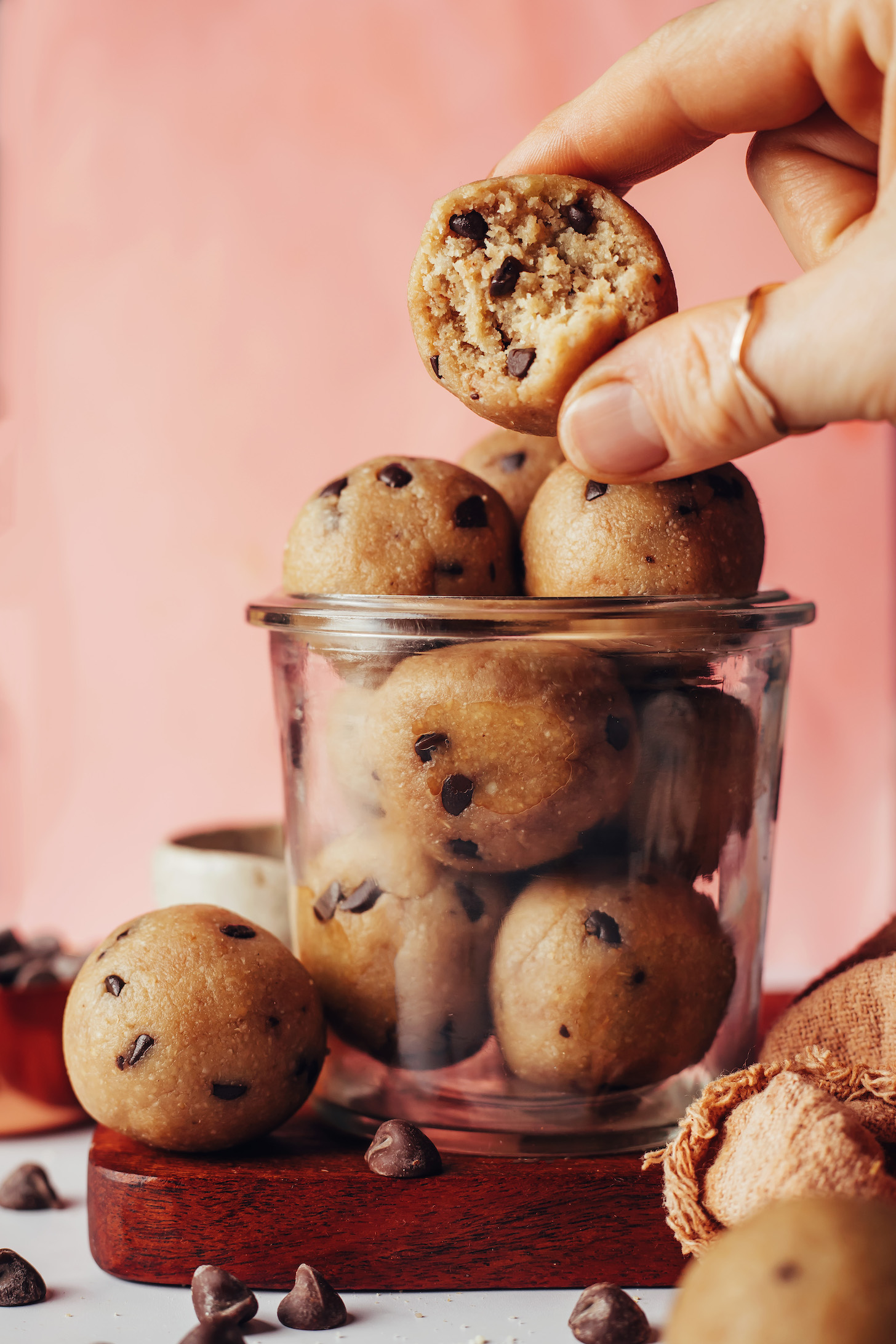 Holding a chocolate chip cookie dough bite over a jar with more energy bites