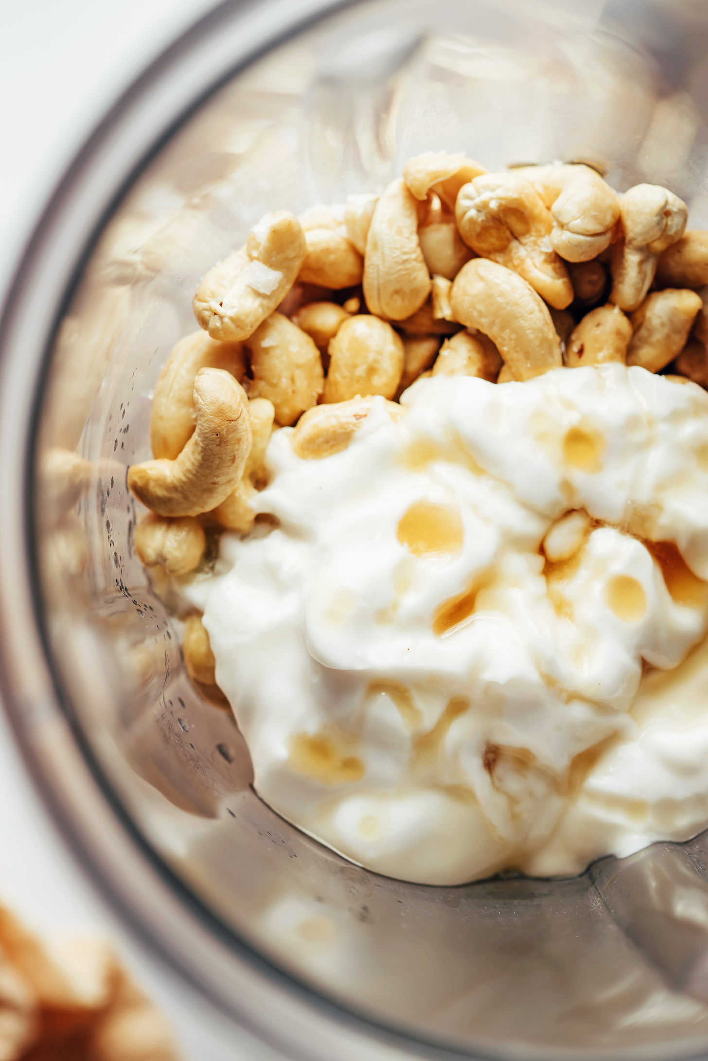 A close up shot of a blender with cashews, coconut yogurt, and maple syrup