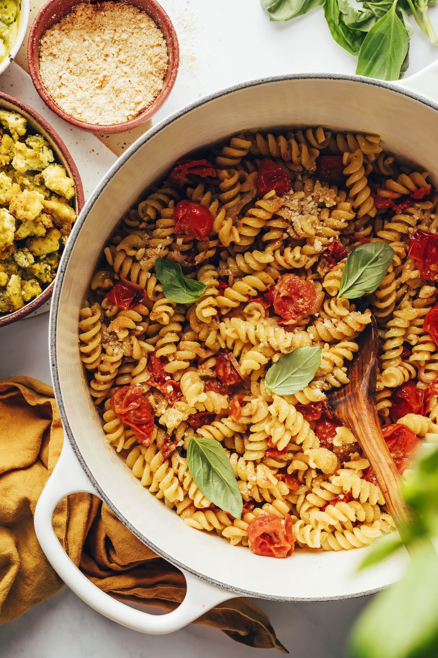 Vegan parmesan cheese and crispy pesto baked tofu next to a pot of our pesto pasta bowls