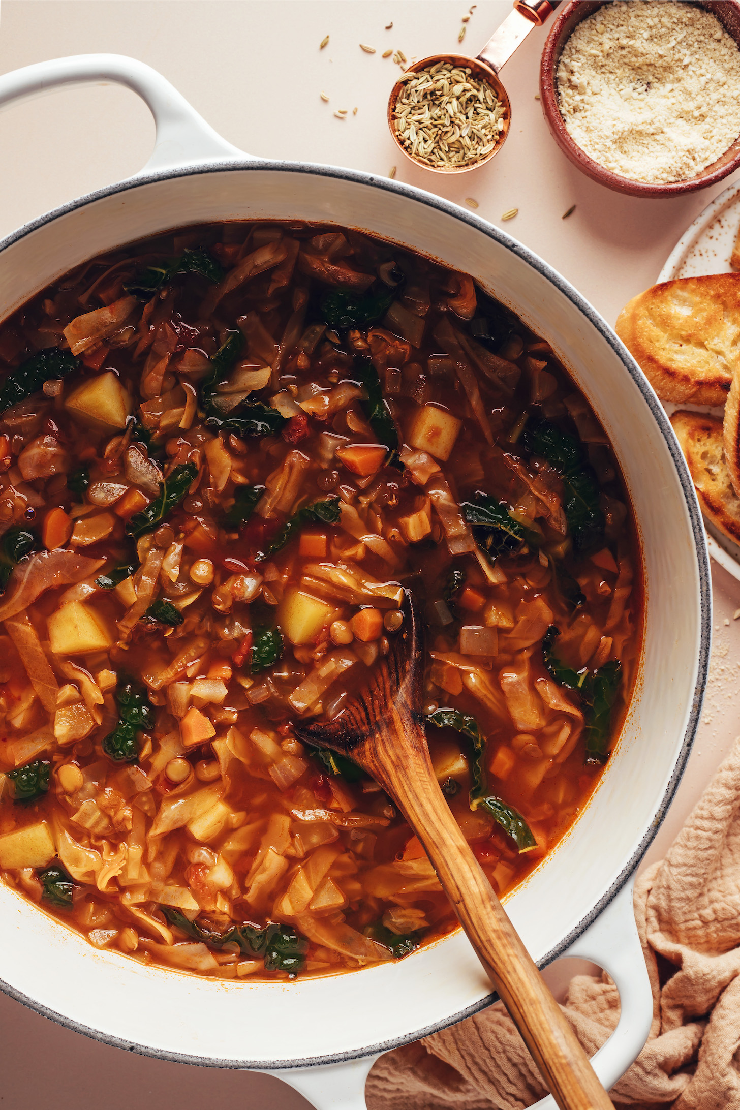Using a wooden spoon to stir a pot of lentil, fennel, and cabbage soup
