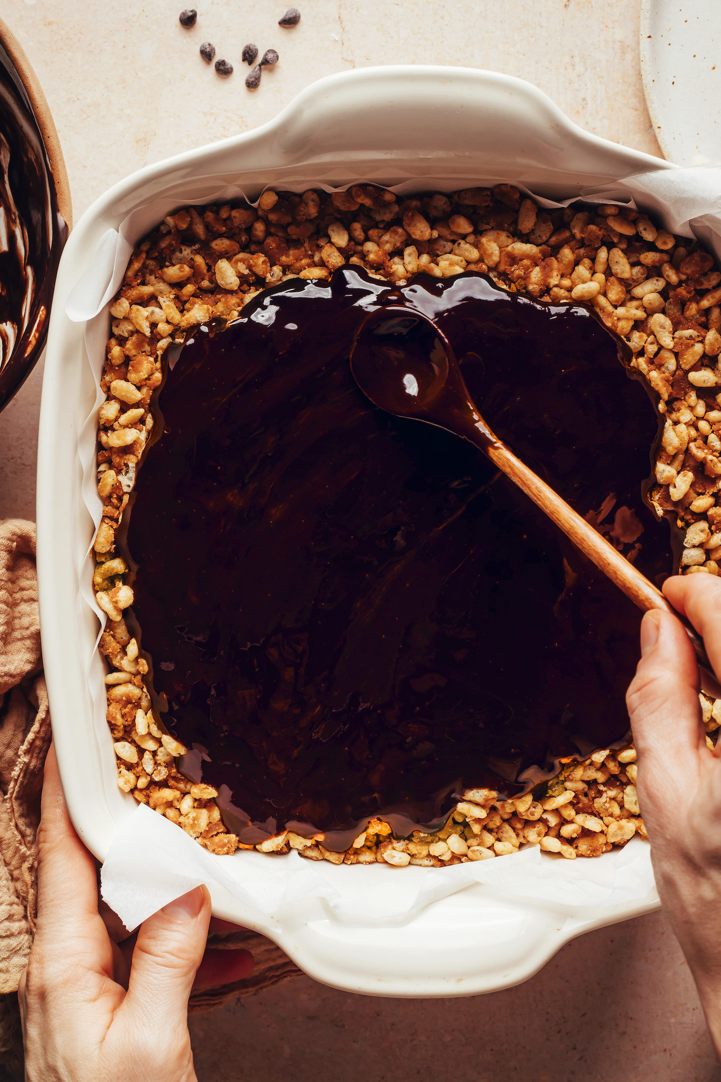 Spreading a melted chocolate ganache mixture over a peanut butter cereal base