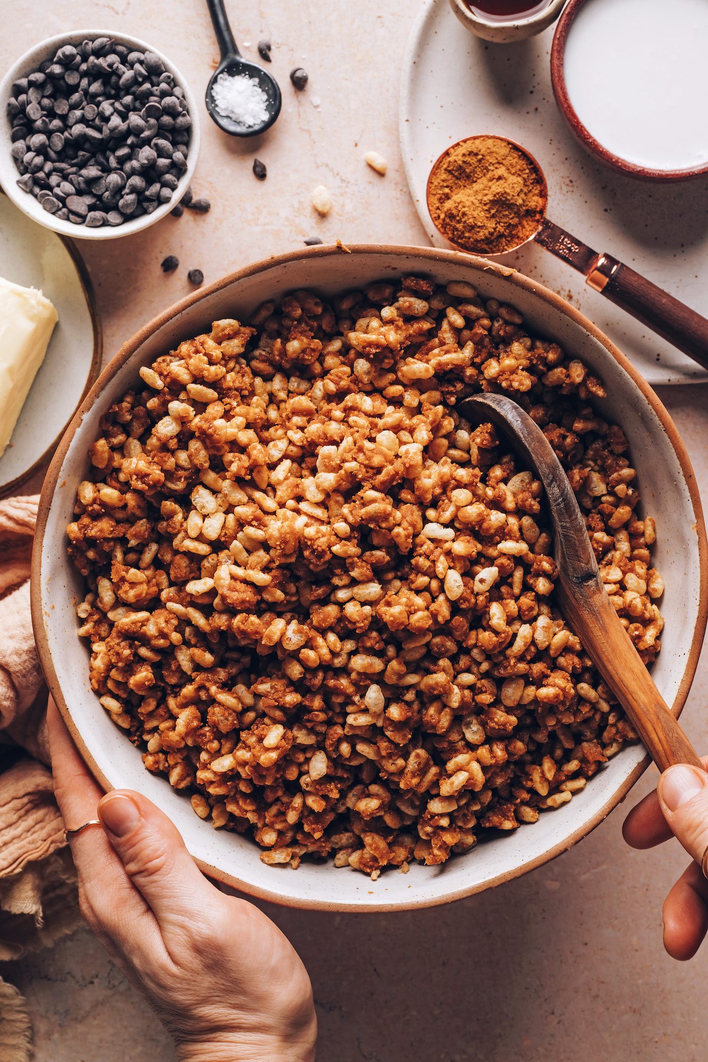 Stirring crispy rice cereal with a maple syrup, coconut sugar, peanut butter, and vanilla mixture