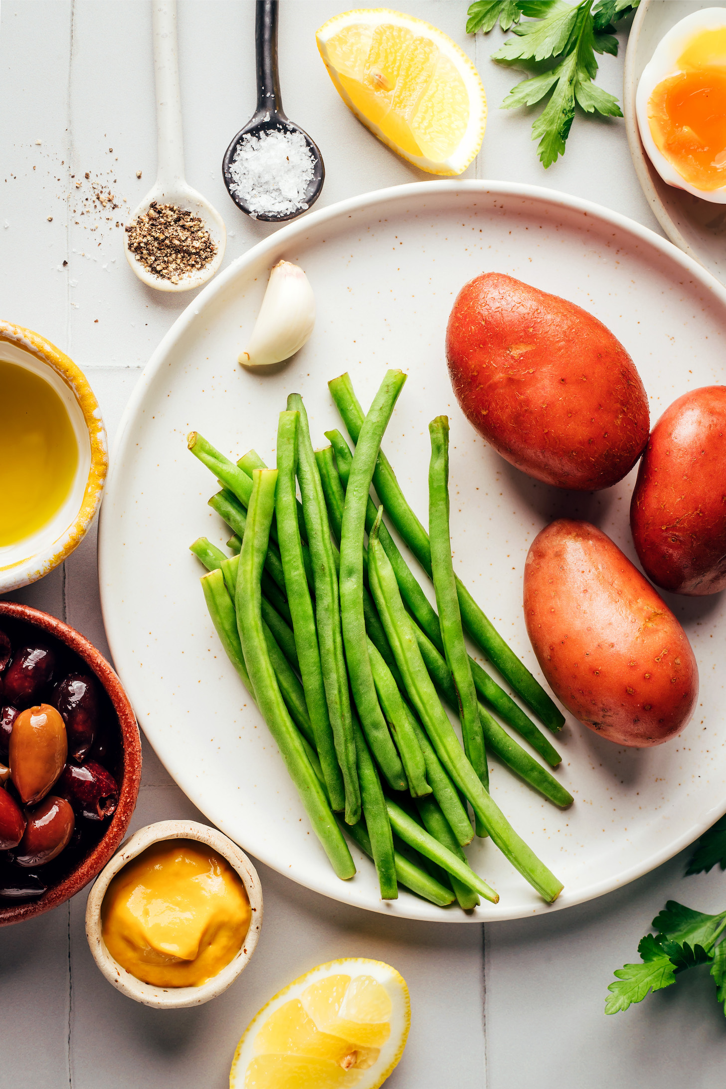 Potatoes, green beans, garlic, lemon, Dijon mustard, kalamata olives, olive oil, black pepper, sea salt, parsley, and egg