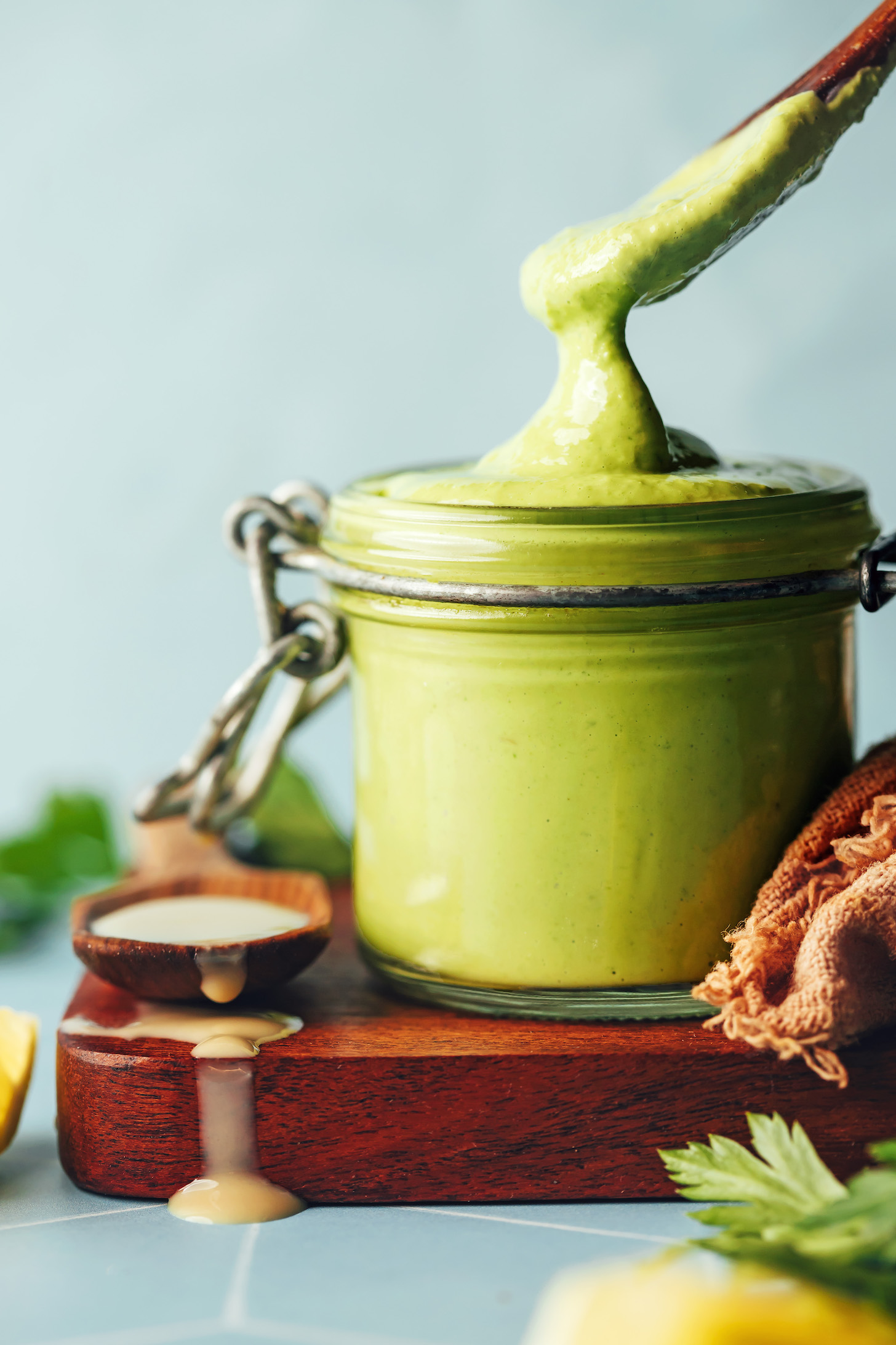Thick, creamy green tahini sauce spilling off a spoon into a glass jar