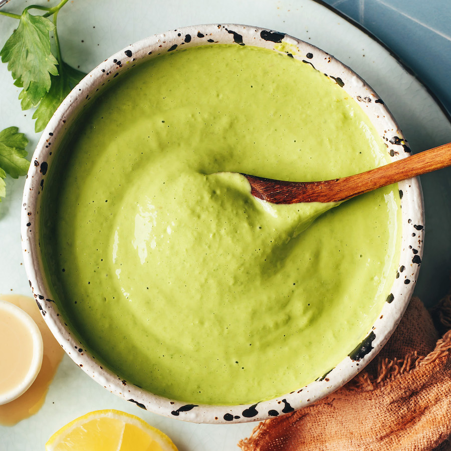 Overhead shot of a spoon in a bowl of herby green tahini sauce