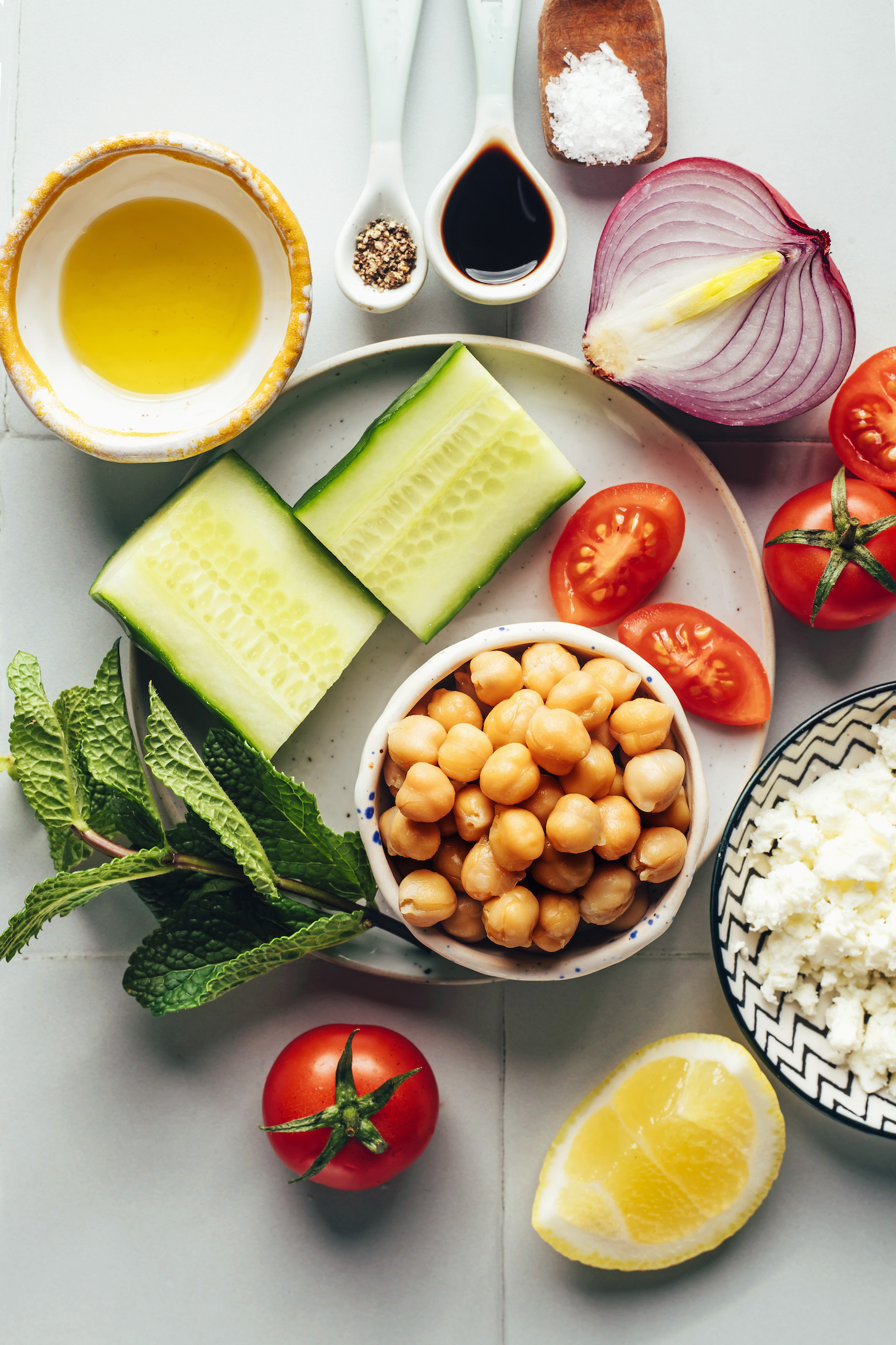 Olive oil, black pepper, balsamic vinegar, salt, red onion, tomato, vegan feta, lemon, chickpeas, mint, and cucumber