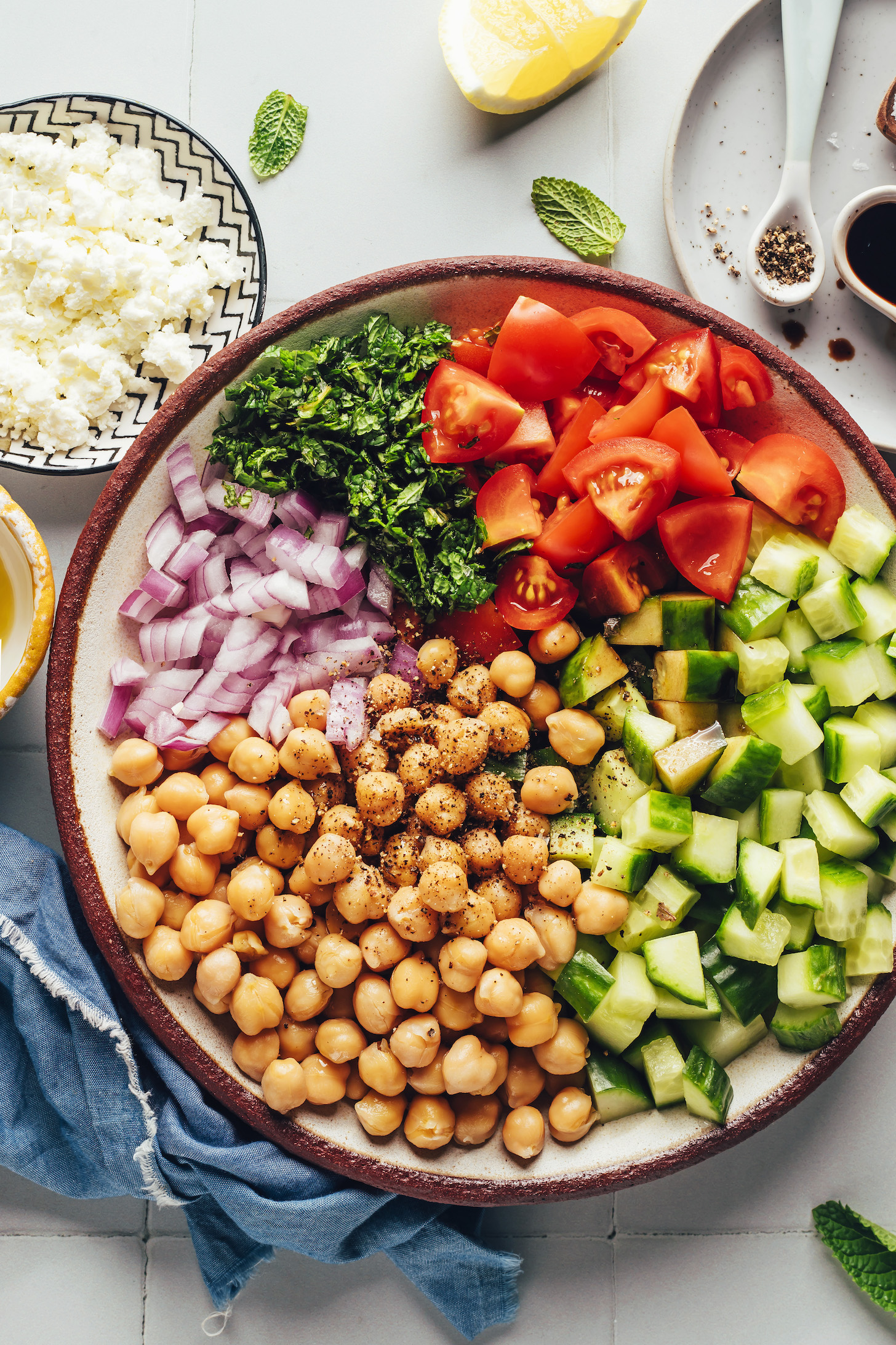 Vegan feta, olive oil, lemon, salt, pepper, balsamic vinegar, and a bowl of chopped cucumber, tomato, parsley, onion, and drained chickpeas