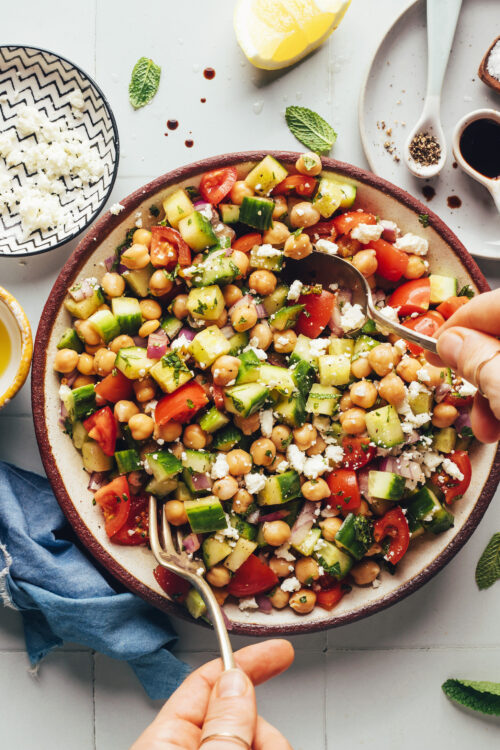 Using a fork and spoon to toss a bowl of Mediterranean cucumber chickpea salad