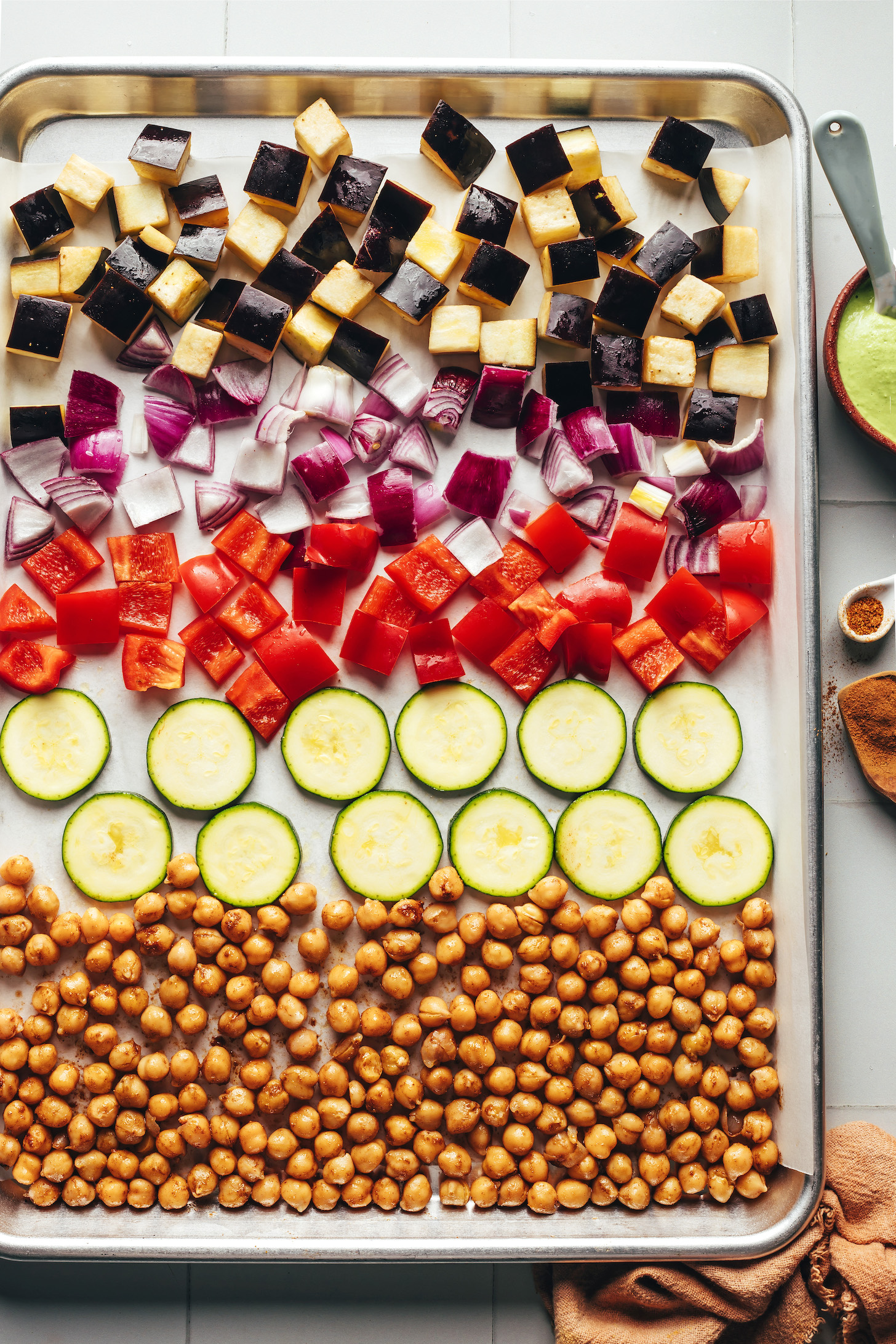 Chopped eggplant, red onion, red bell pepper, zucchini, and chickpeas on a baking sheet