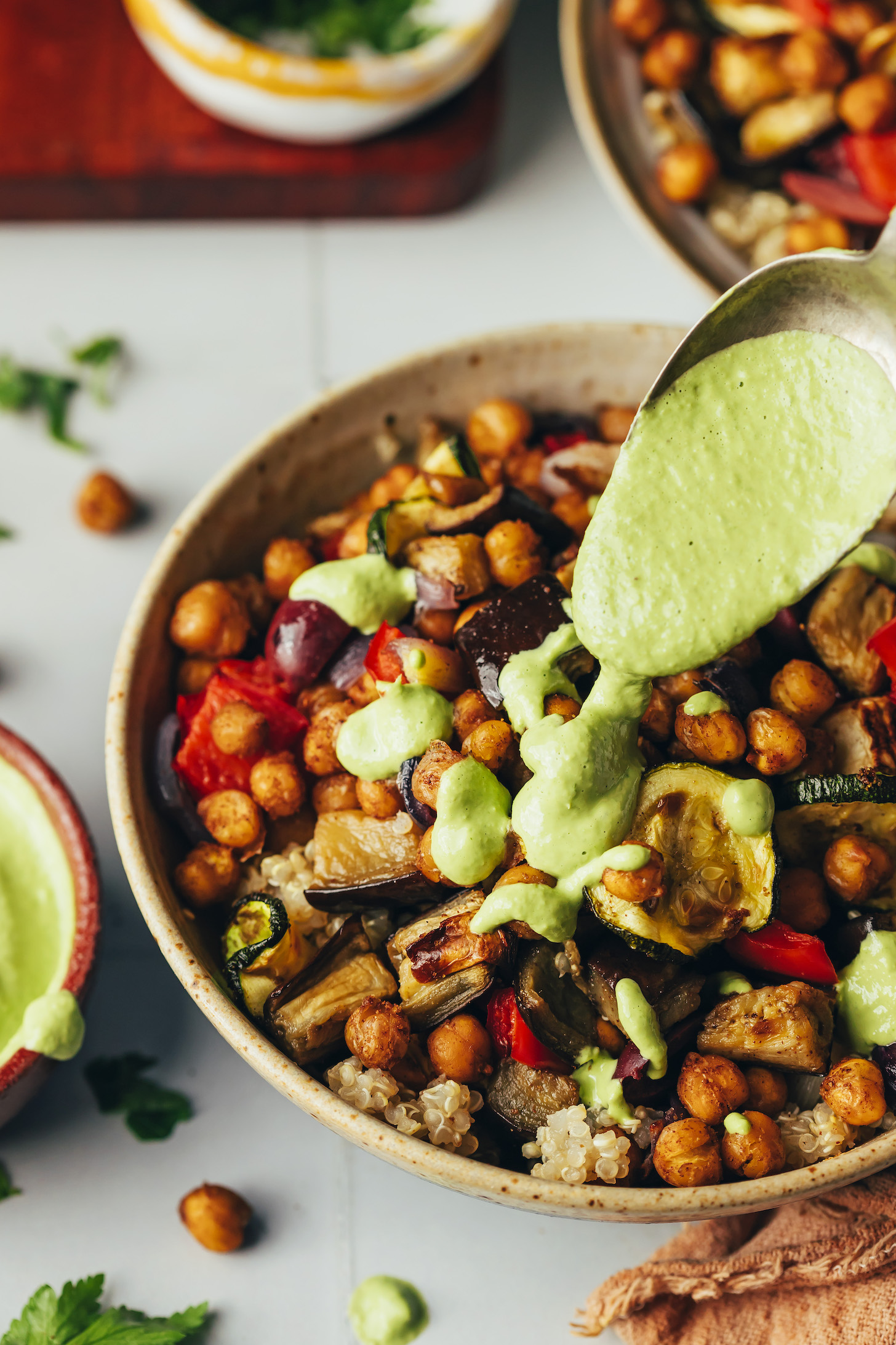 Drizzling green tahini sauce from a spoon onto a veggie and grain bowl