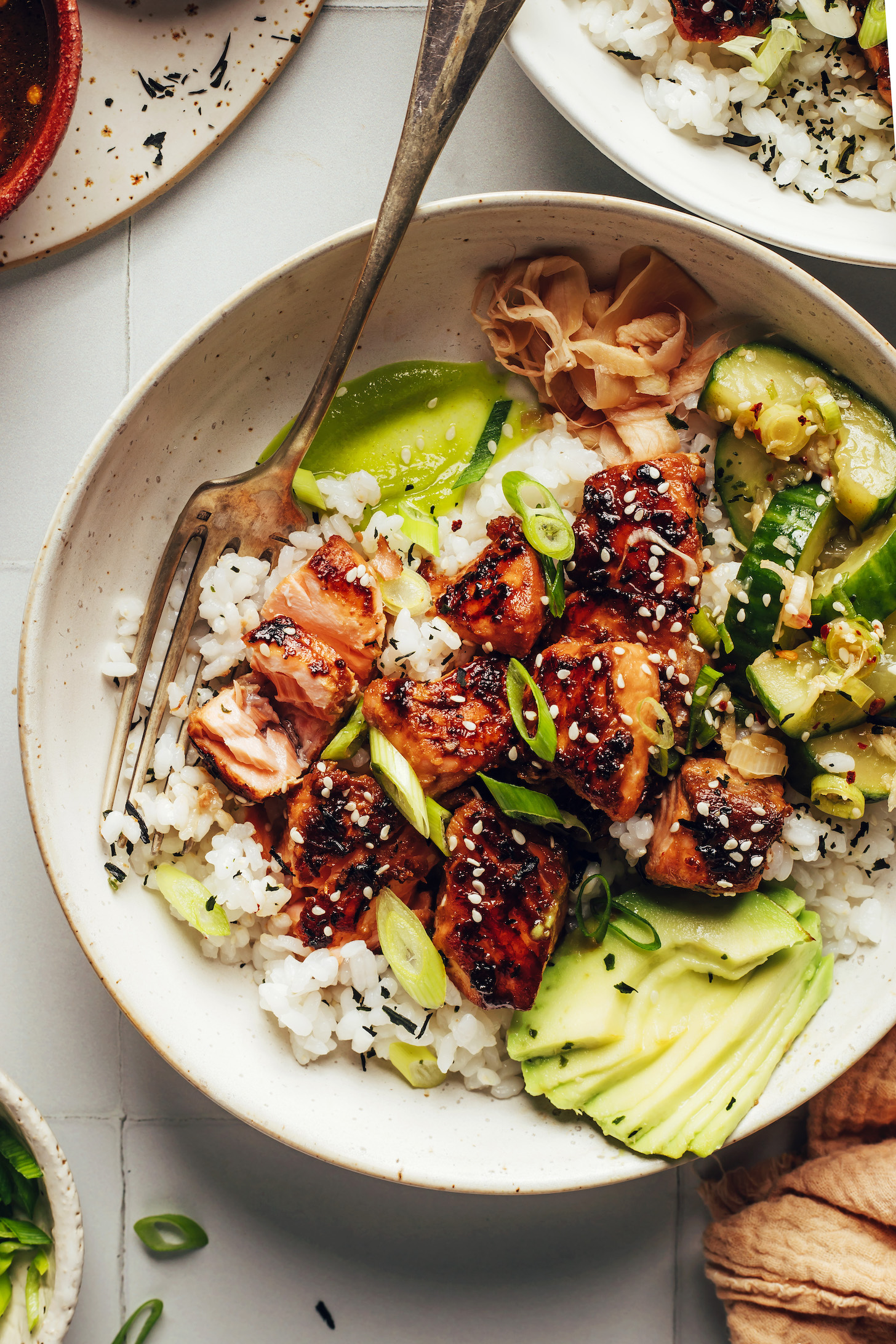 Tamari-glazed salmon, rice, avocado, cucumber salad, and other sushi bowl ingredients in a large bowl