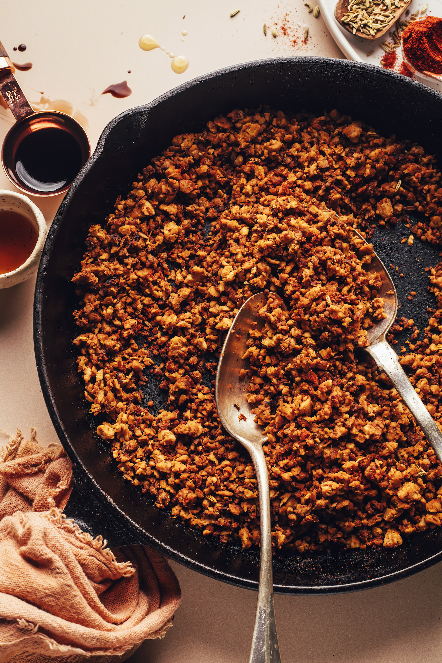 Serving spoons in a skillet of vegan Italian sausage crumbles