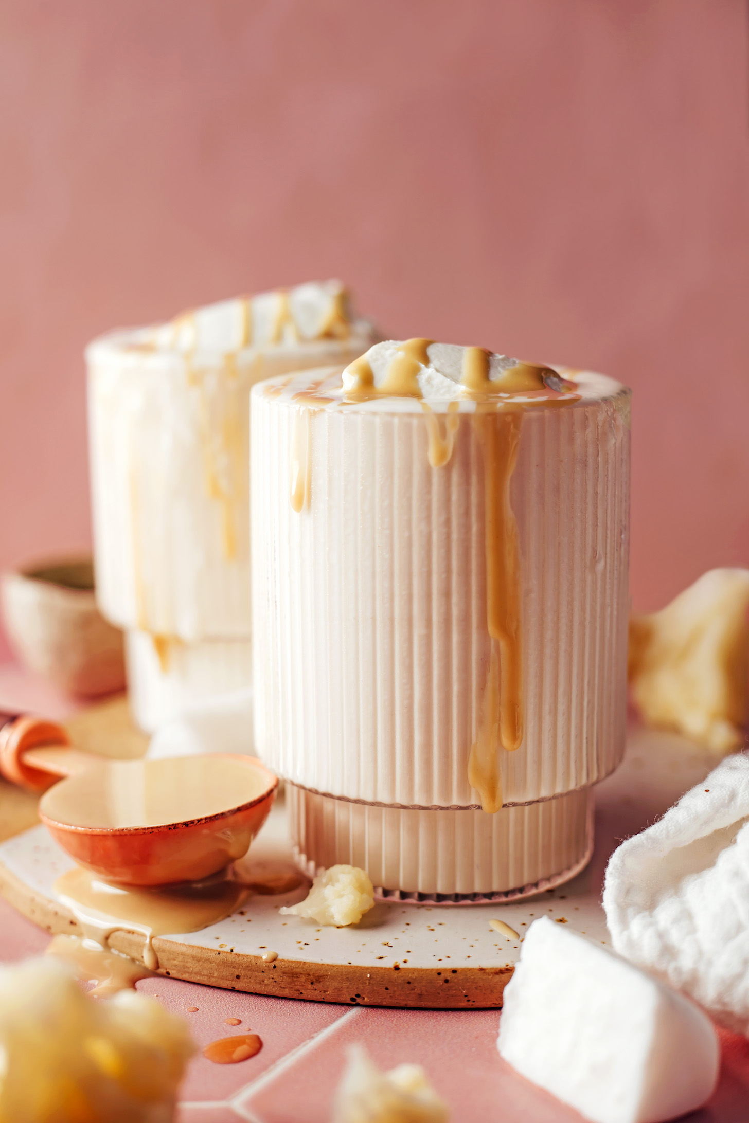 Spoonful of tahini next to overflowing glasses of vanilla tahini shakes