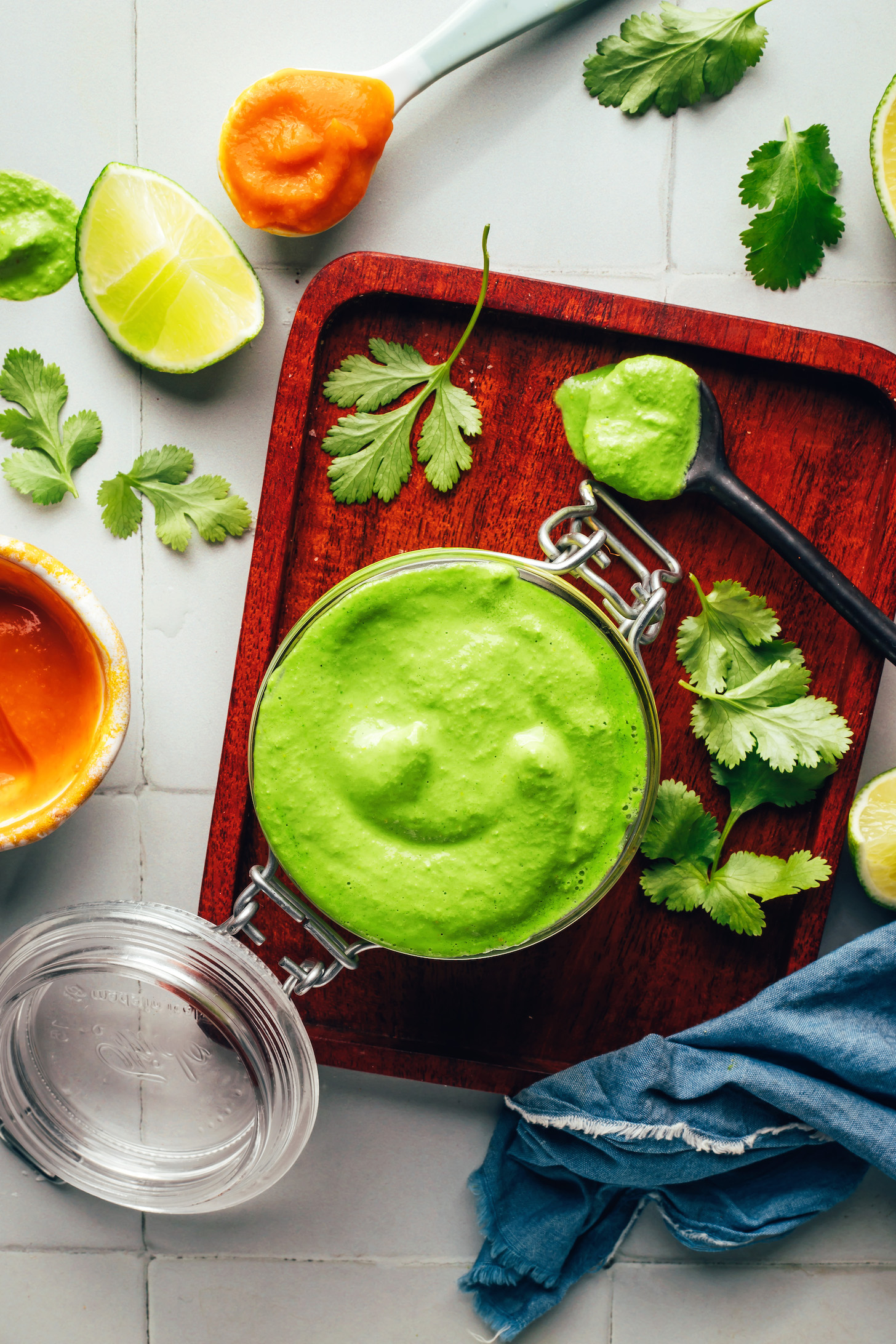 Overhead shot of a jar of homemade aji verde next to cilantro, lime, and aji amarillo paste