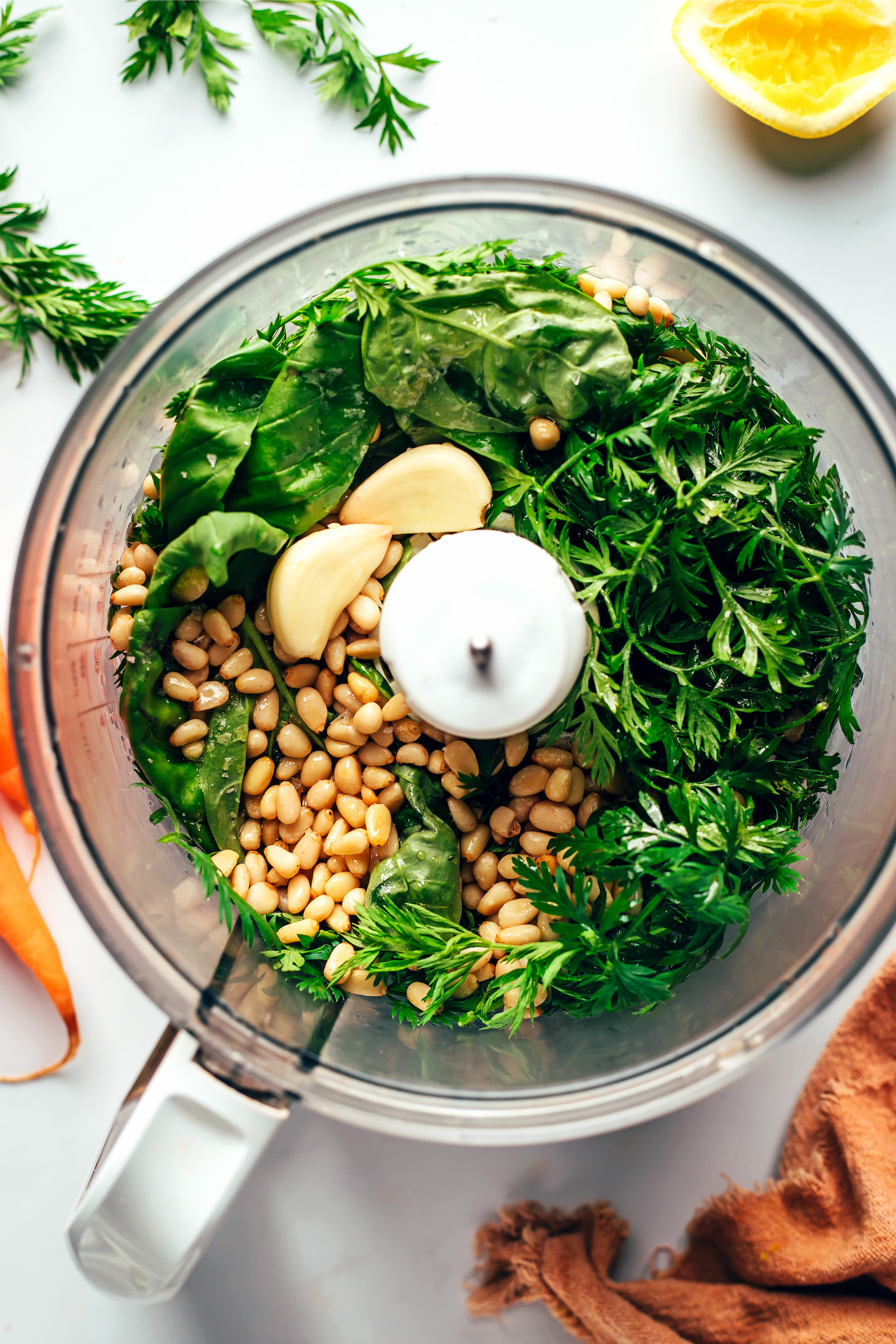 Food processor with basil, carrot tops, salt, and pine nuts