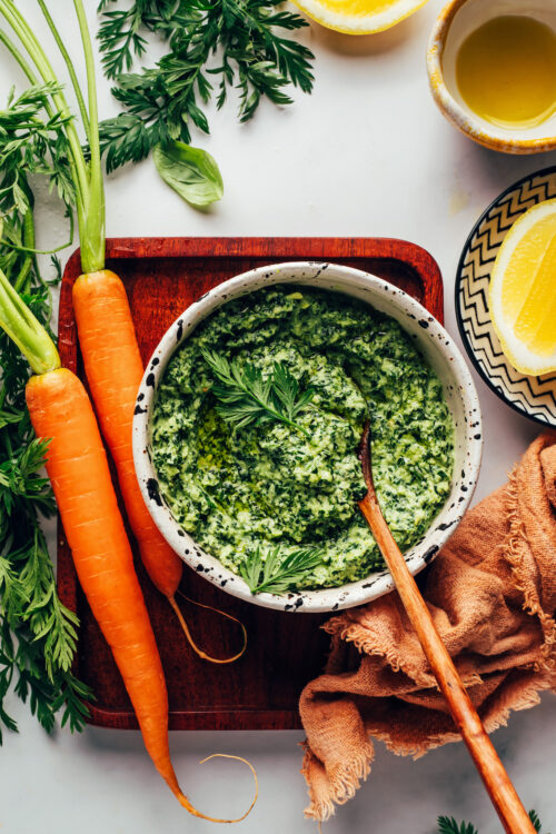 Carrots next to a bowl of carrot top pesto