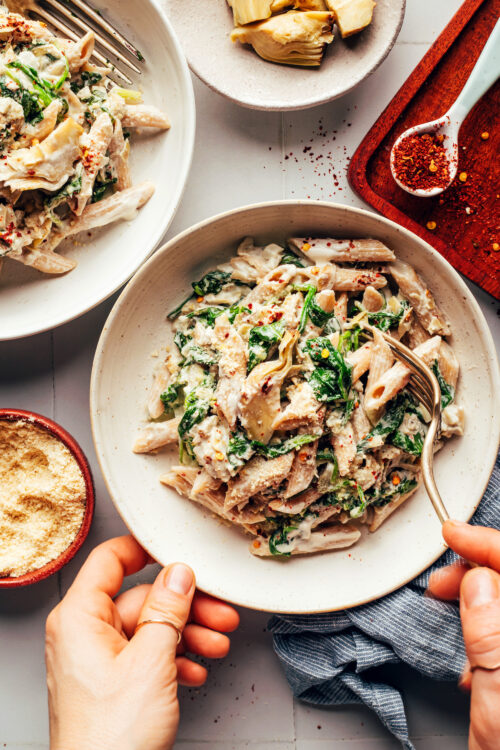 Using a fork to grab a bite of vegan spinach artichoke pasta