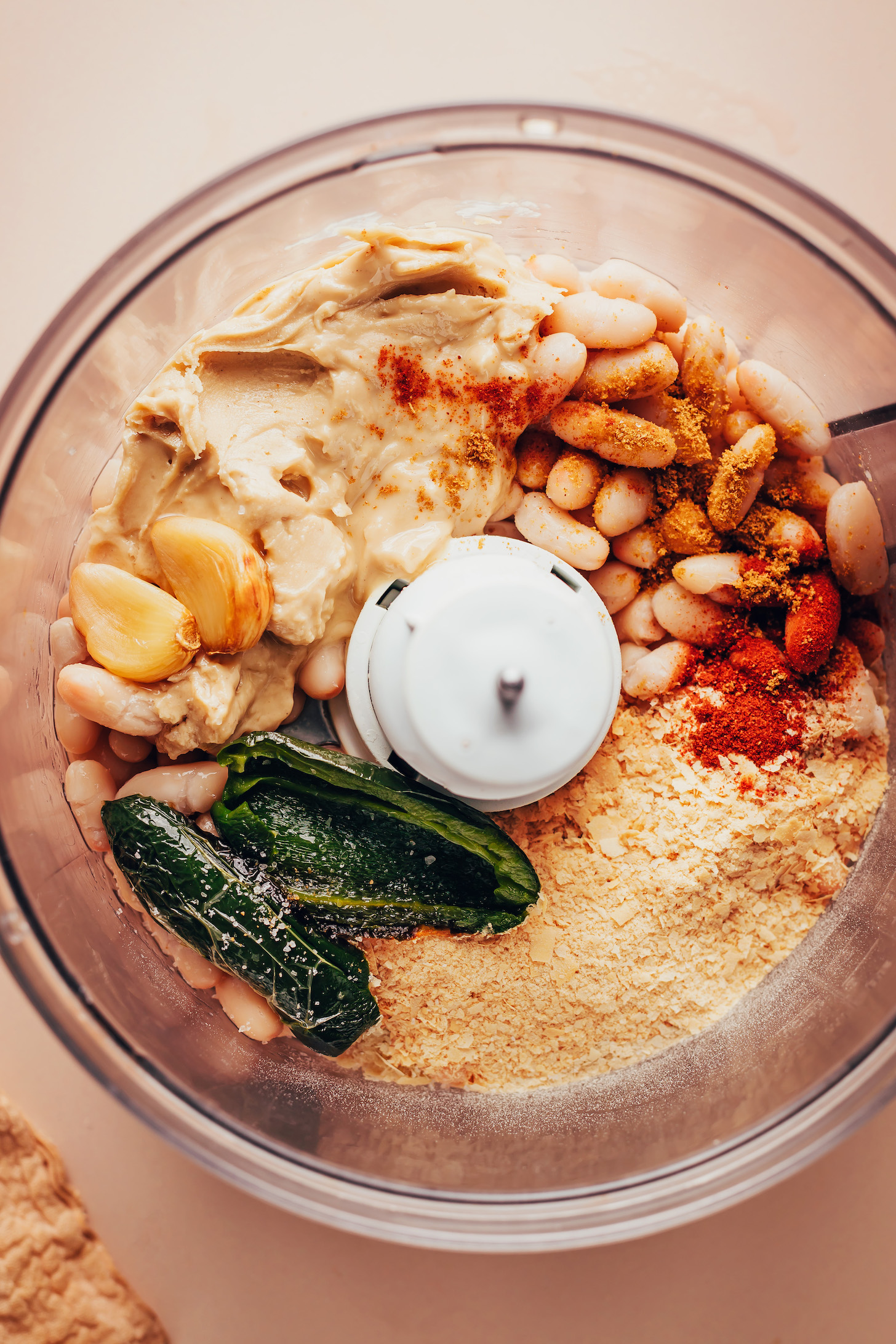 Food processor with white beans, cashew butter, garlic, jalapeño, nutritional yeast, and smoked paprika