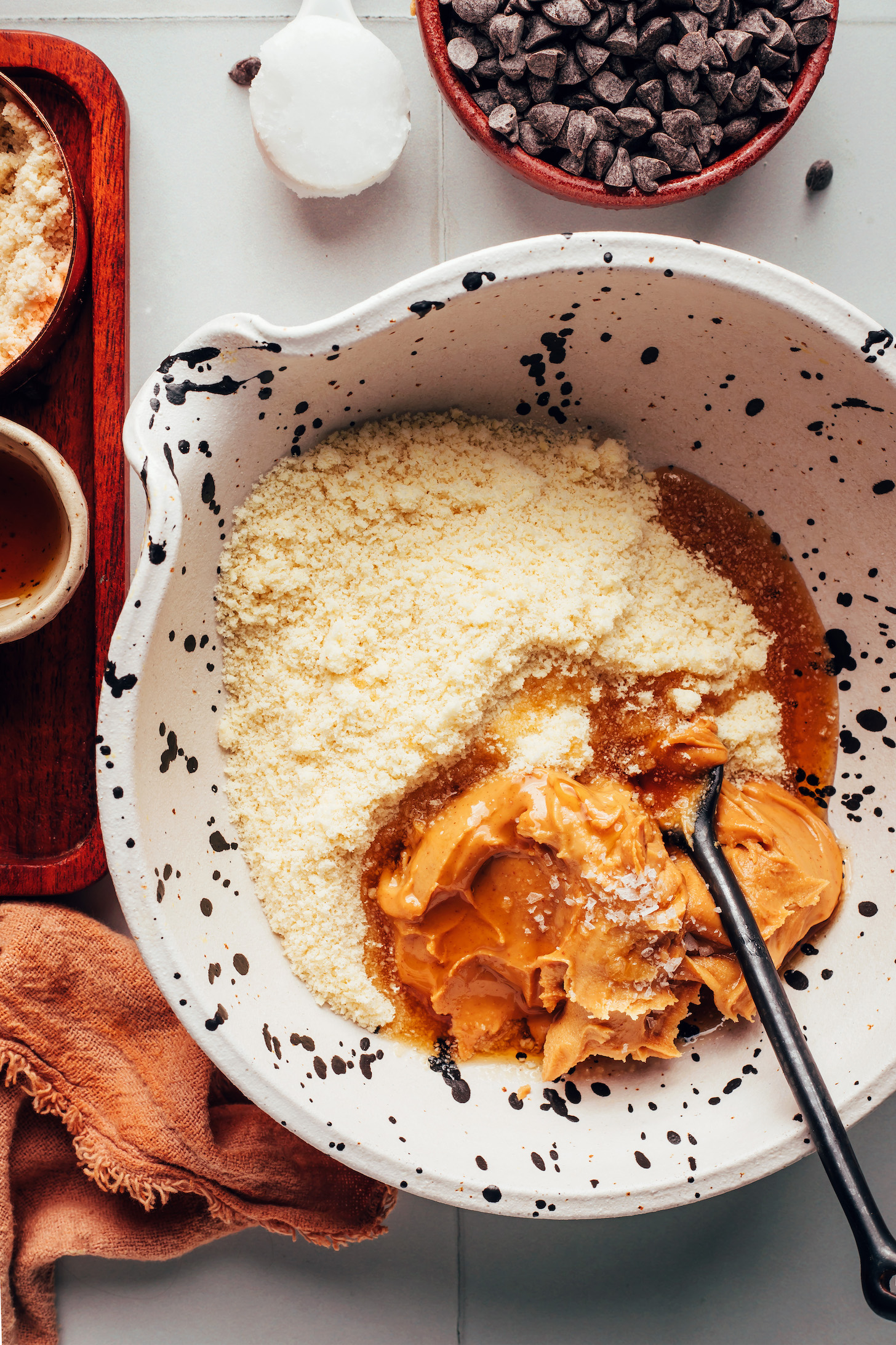 Spoon in a bowl with almond flour, peanut butter, maple syrup, and sea salt