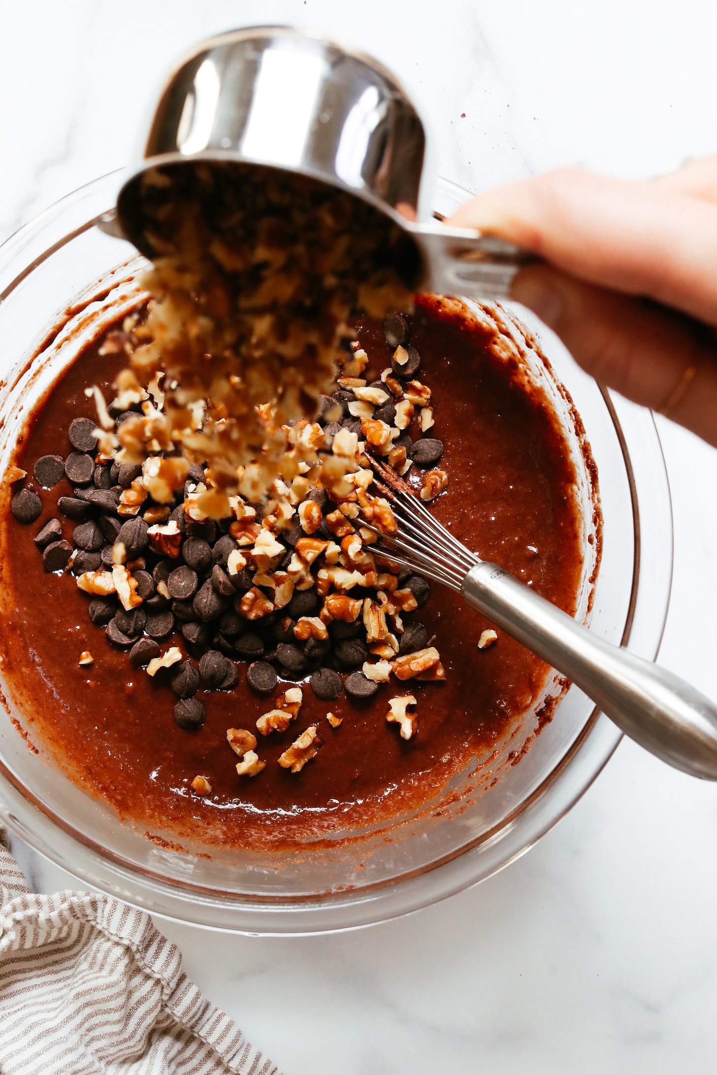 Pouring walnuts over chocolate chips in a bowl of chocolate banana nut muffin batter