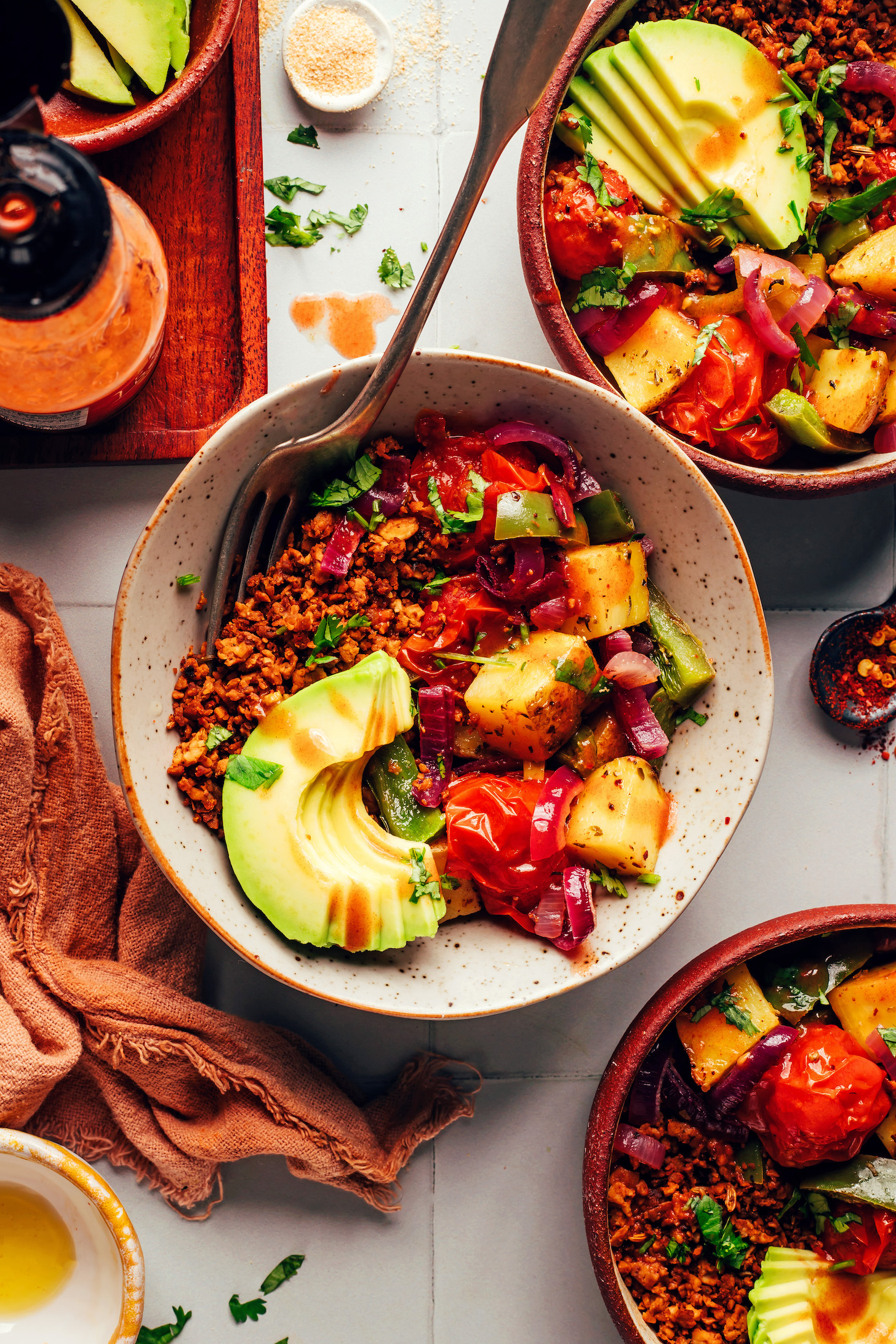 Vegan breakfast bowls with tempeh sausage crumbles, roasted veggies, avocado, parsley, and hot sauce
