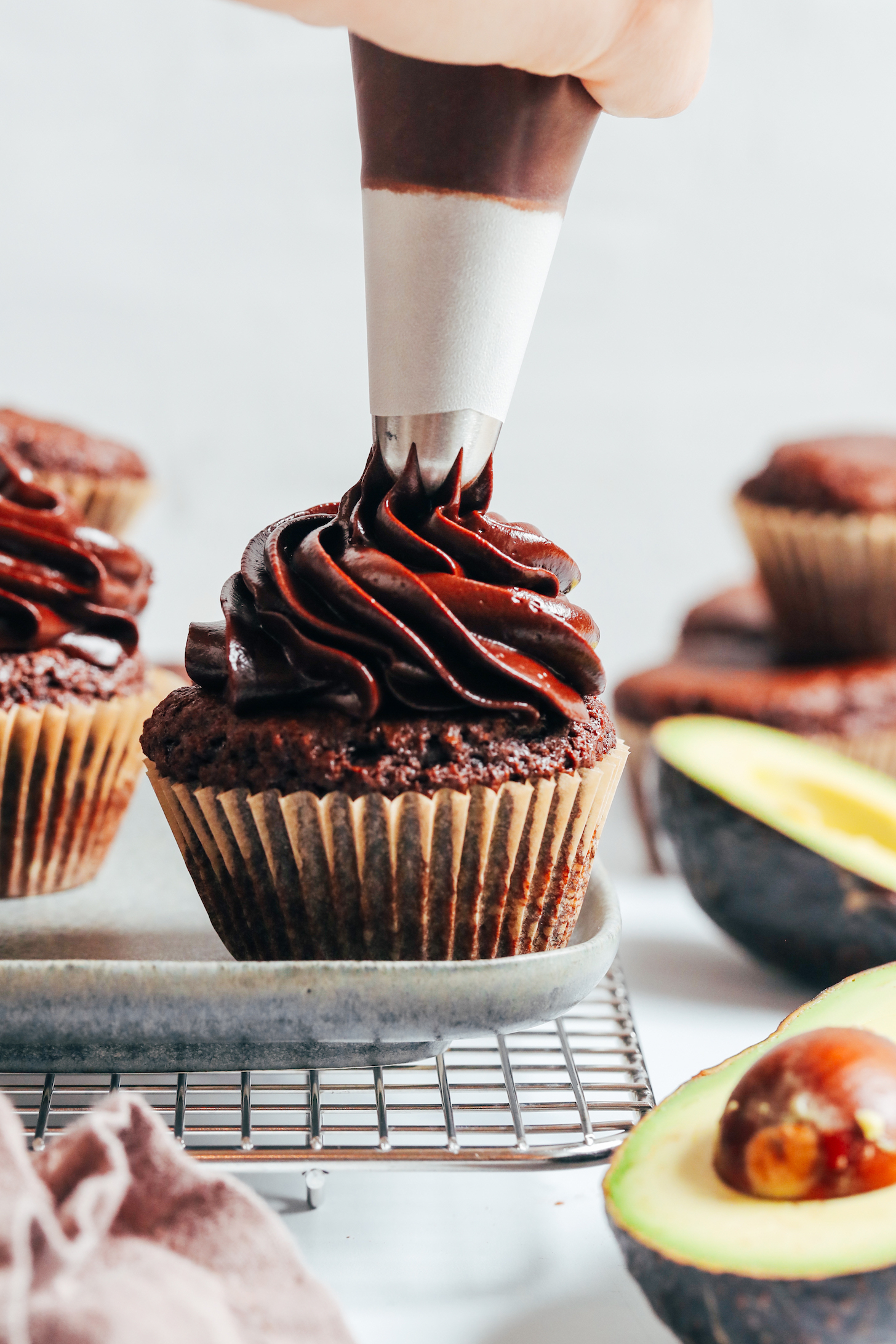 Piping vegan chocolate avocado frosting onto a chocolate cupcake