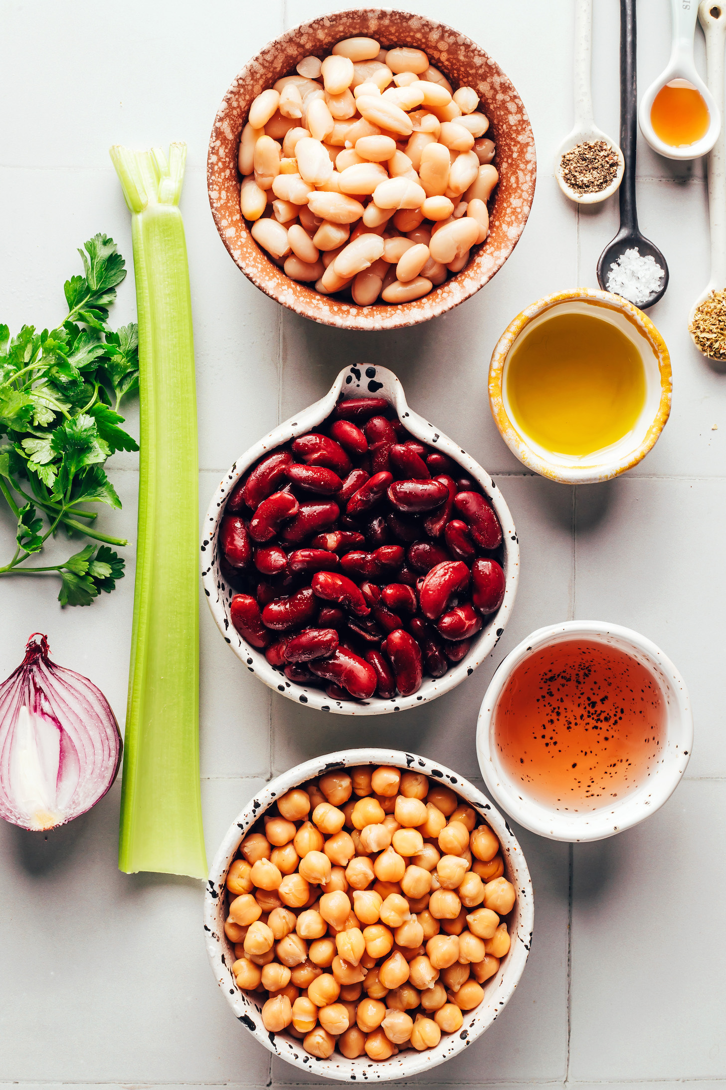 Parsley, red onion, celery, white beans, kidney beans, chickpeas, red wine vinegar, olive oil, salt, pepper, maple syrup, and dried oregano