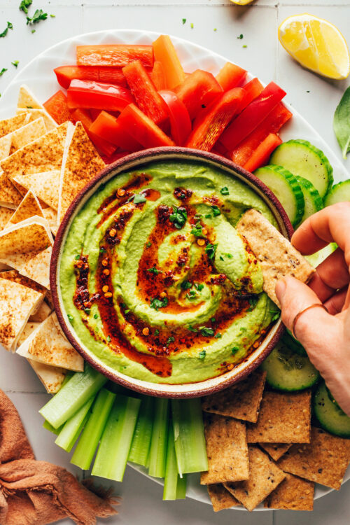 Dipping a cracker into a bowl of herby green goddess hummus