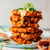 Stack of kimchi rice fritters topped with sriracha sour cream, green onions, and cilantro