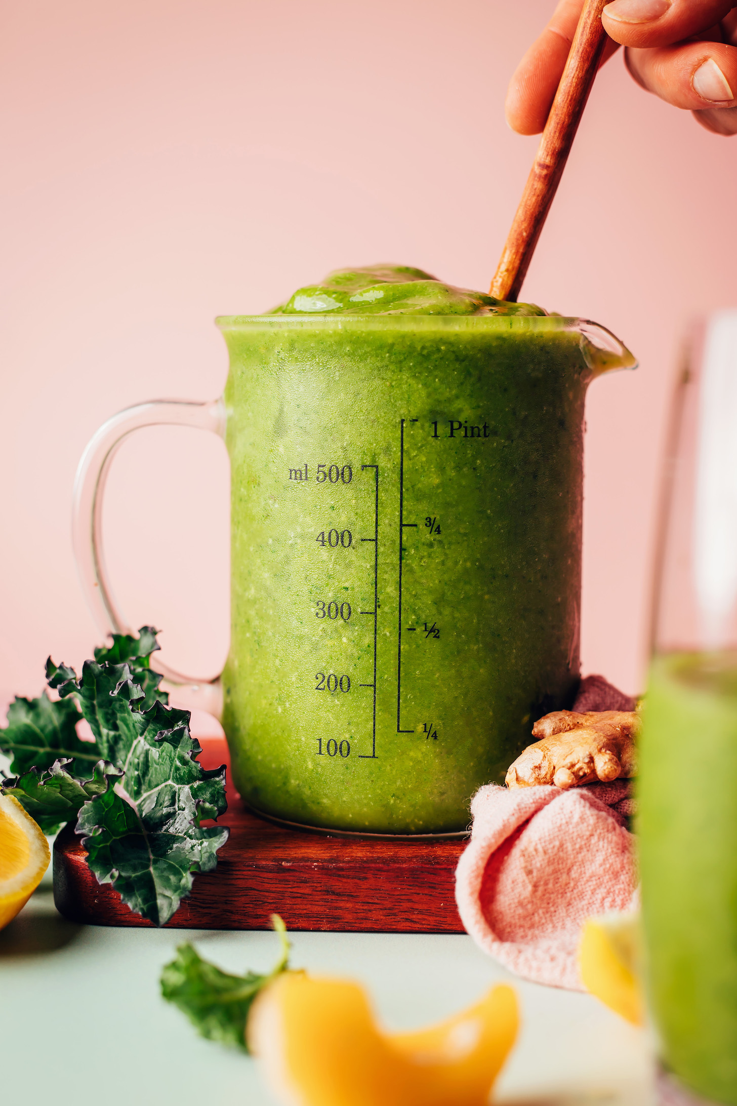 Measuring glass filled with our Mango Ginger Kale Smoothie recipe next to ingredients used to make it