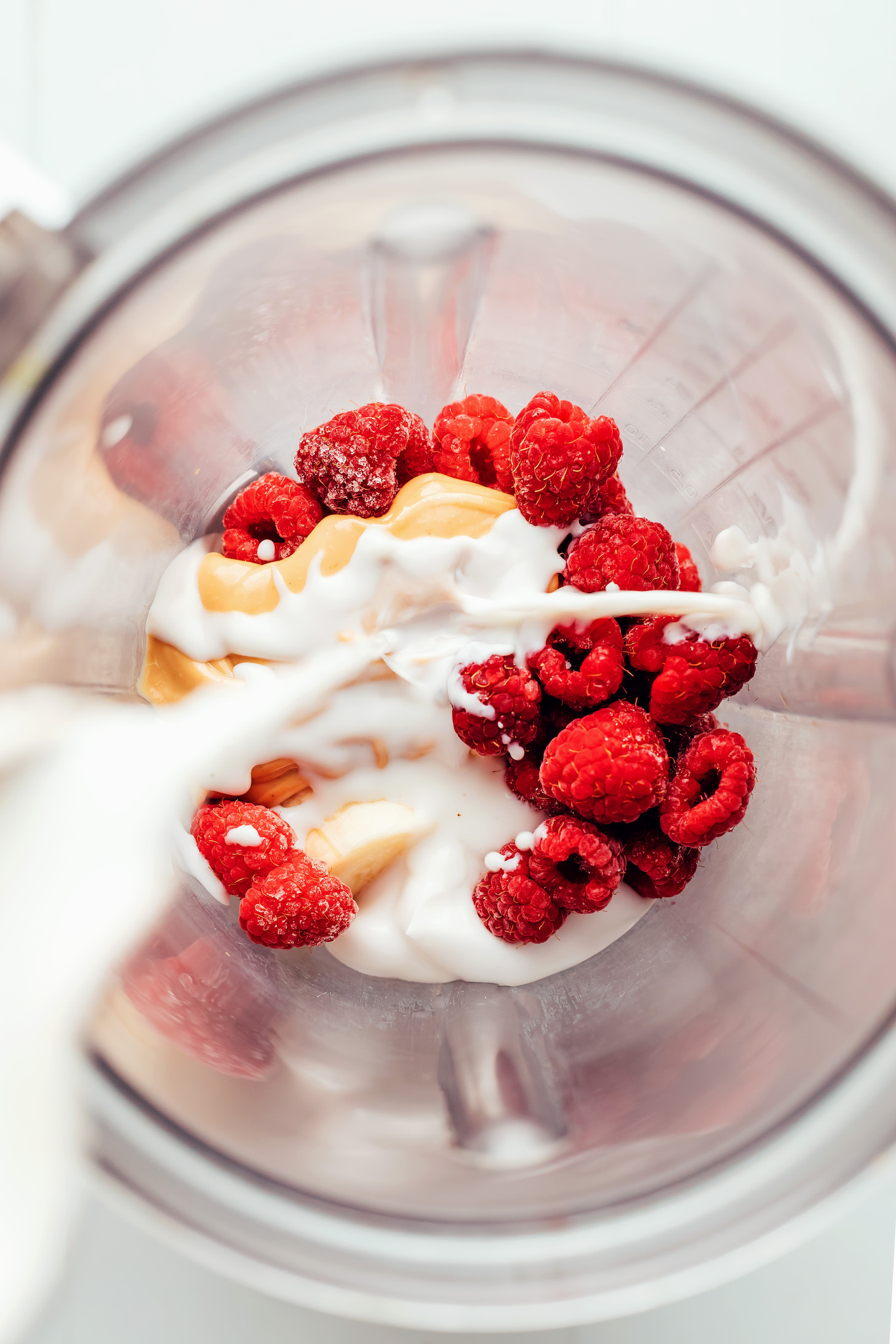 Overhead shot of adding dairy-free milk into a blender with cashew butter, banana, and raspberries