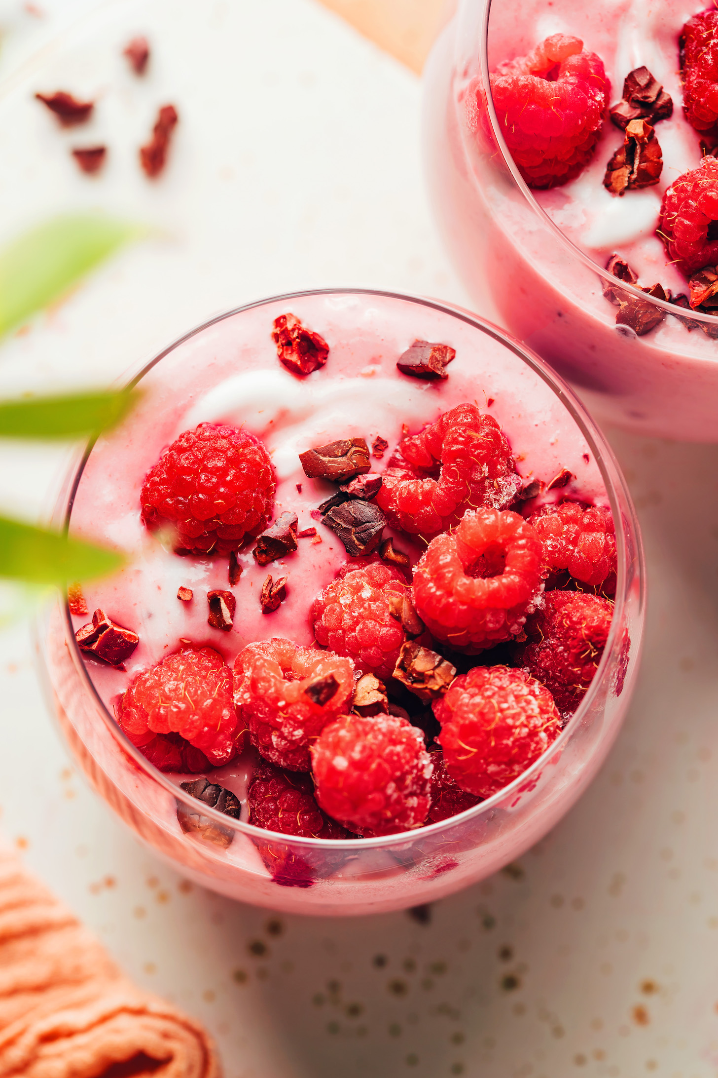 Overhead shot of two glasses of our raspberry banana smoothie recipe topped with raspberries and cacao nibs