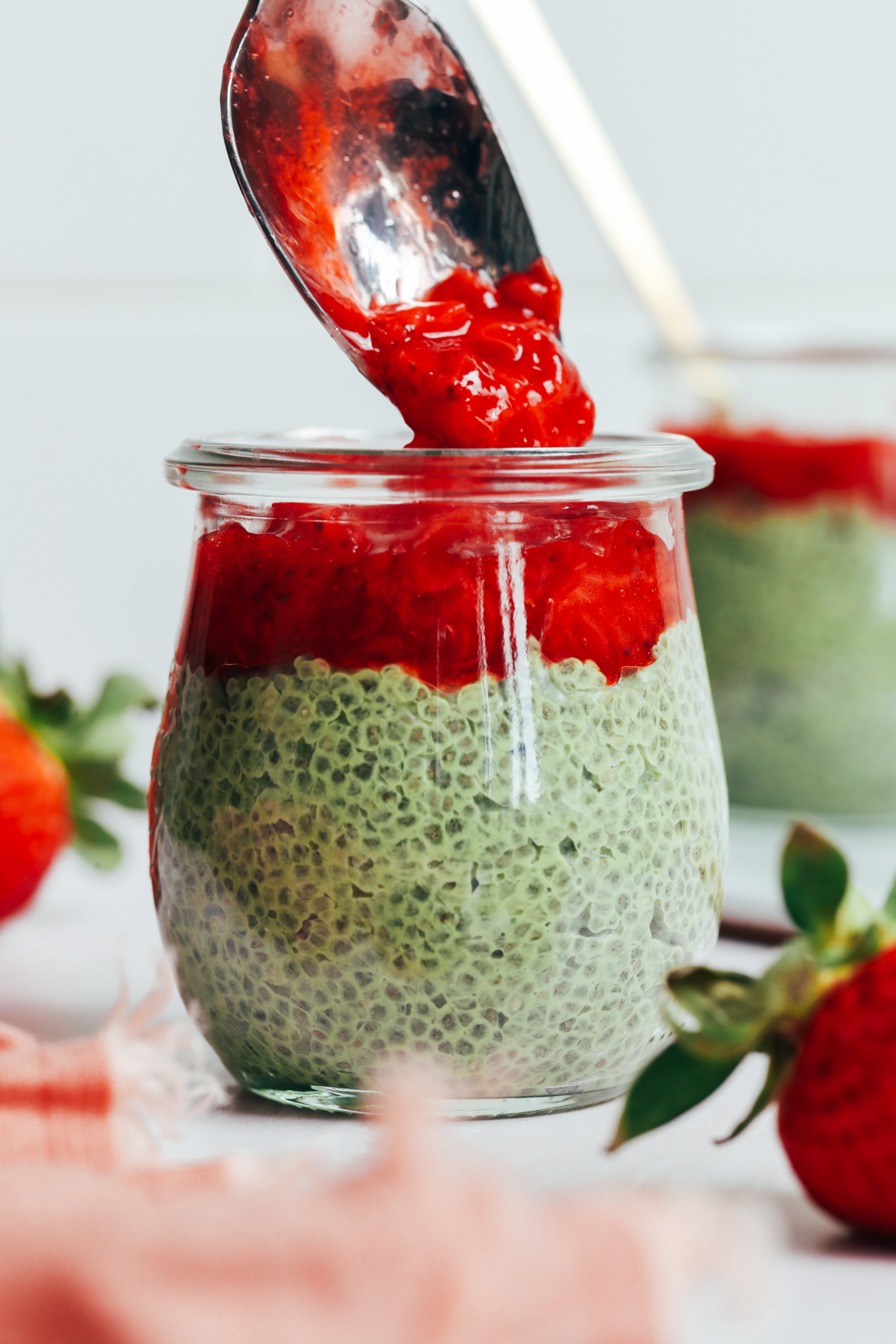 Using a spoon to top a jar of matcha chia pudding with strawberry compote