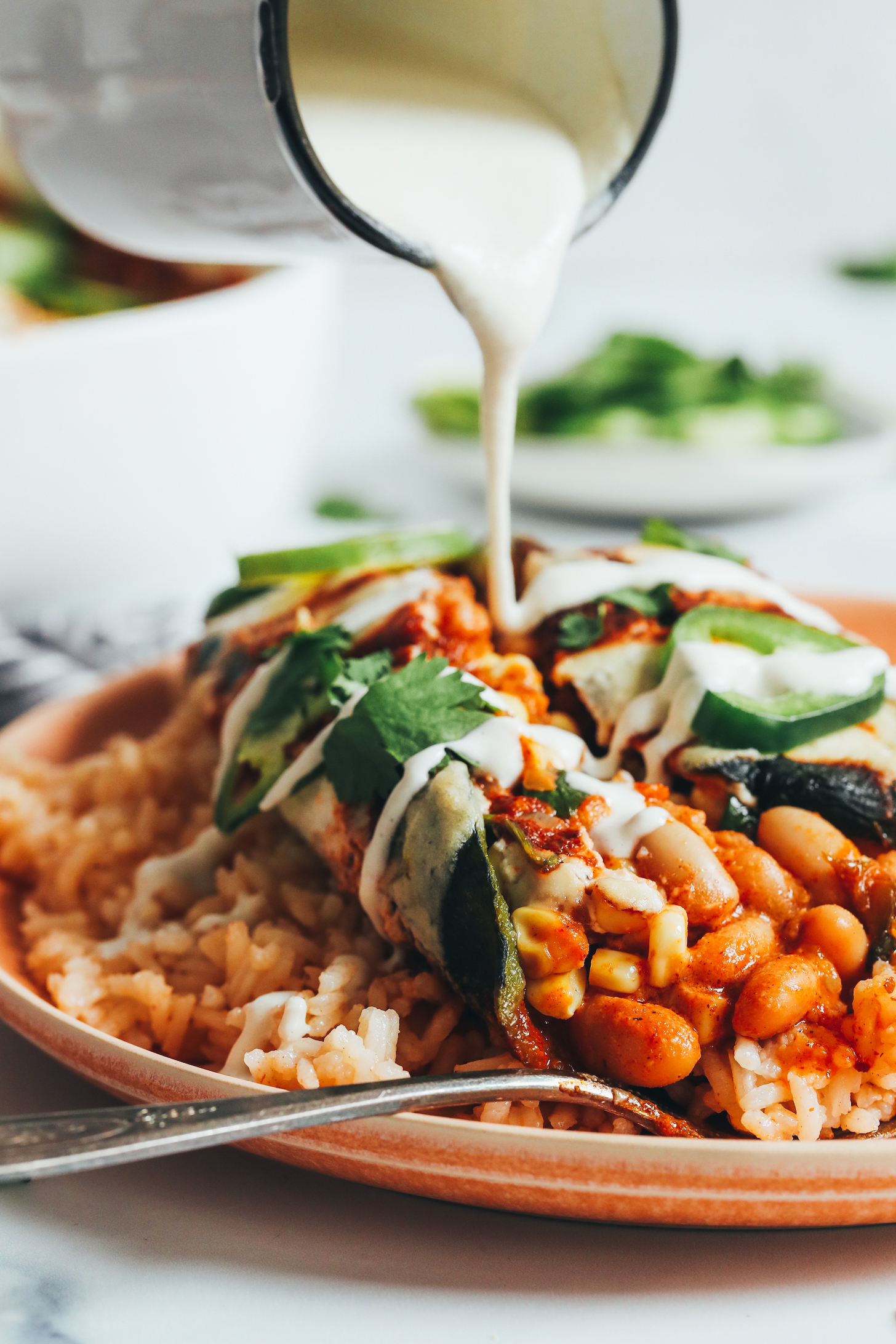 Drizzling a cashew cream sauce onto a vegan white bean chile relleno