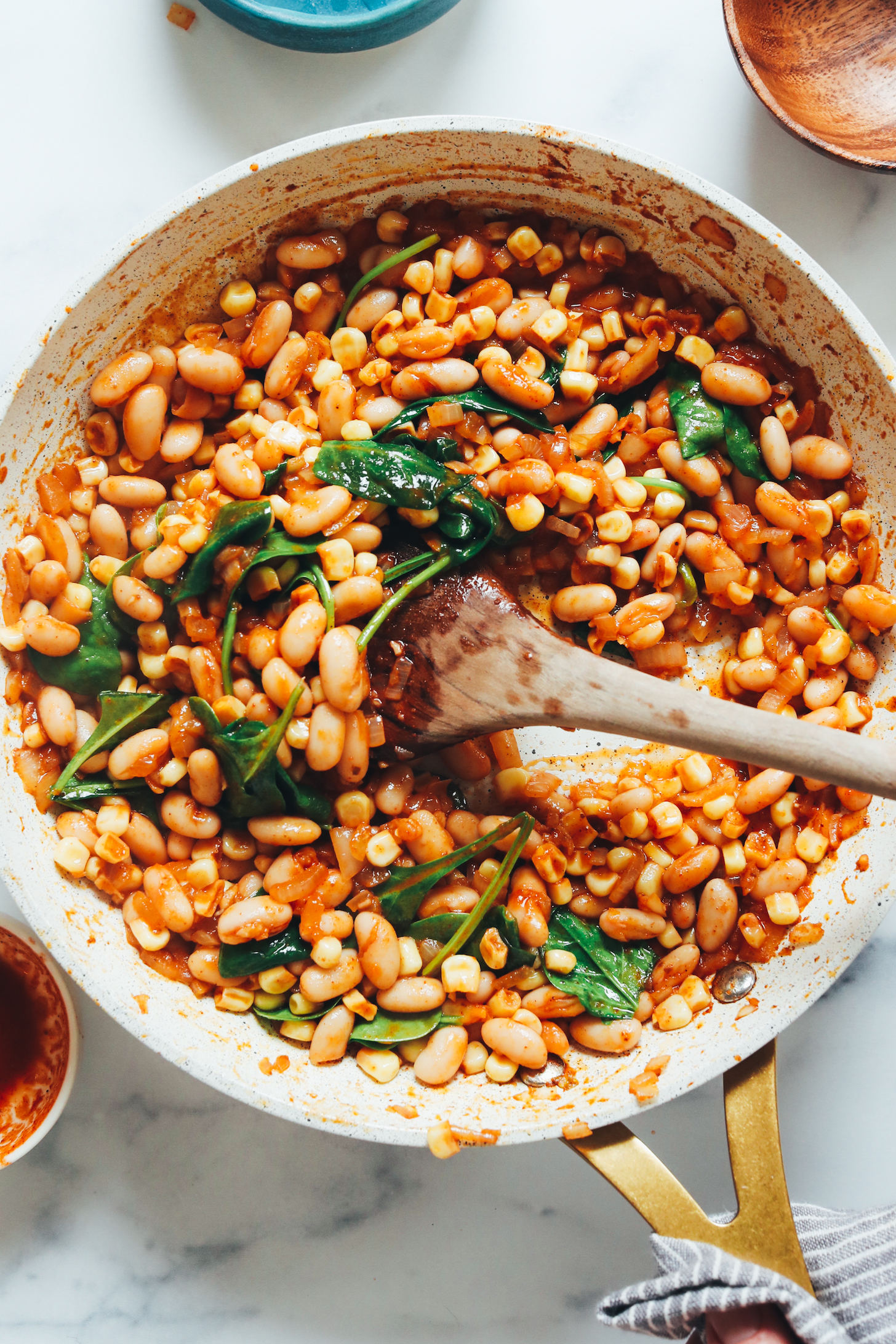Sautéing white beans, onions, corn, enchilada sauce, and spinach in a skillet