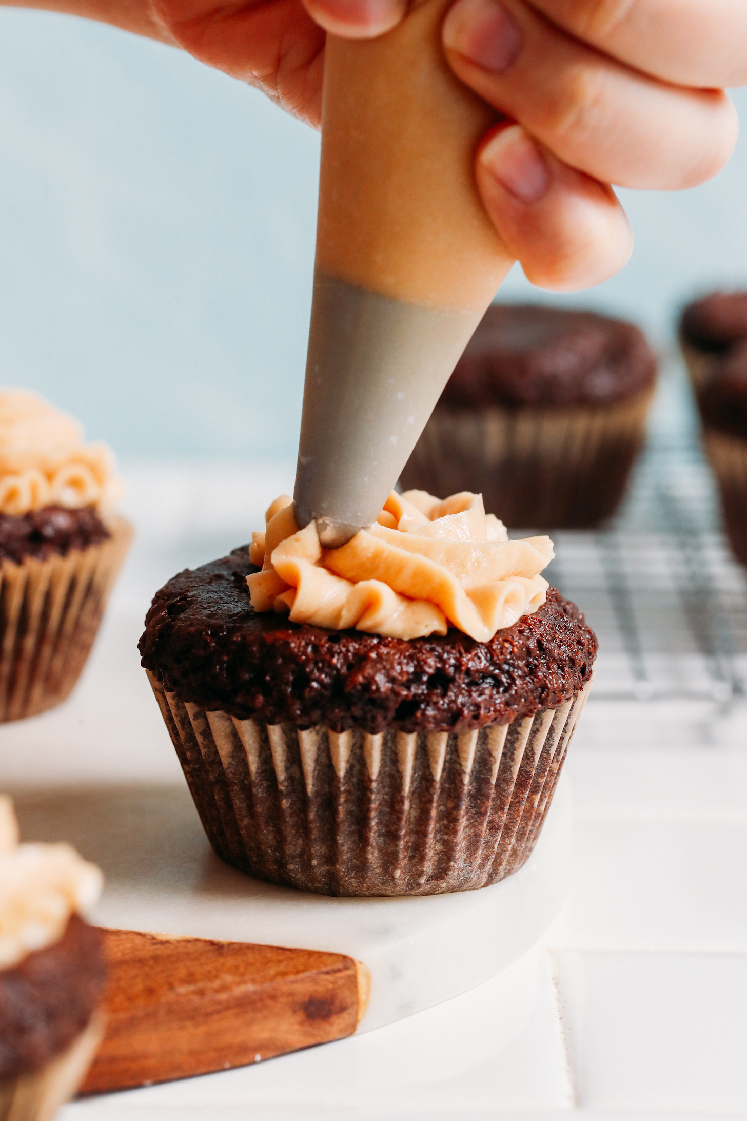 Piping vegan peanut butter frosting onto a cupcake