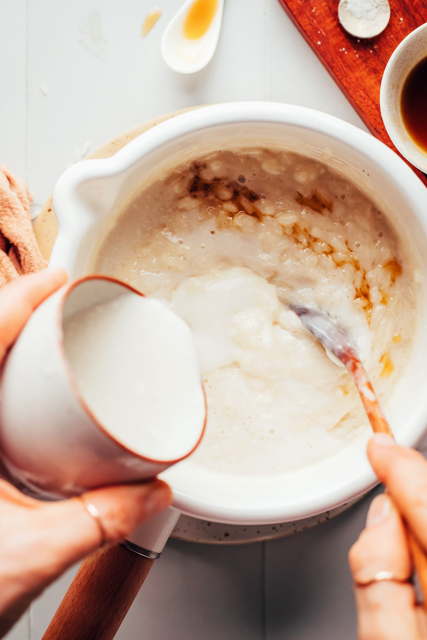 Pouring coconut milk into a pot with maple syrup, vanilla, almond milk, and cooked white rice