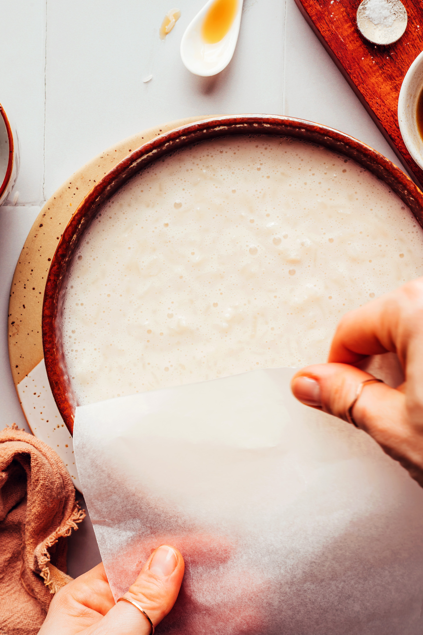 Placing parchment paper over a bowl of rice pudding to prevent a film from forming on the top