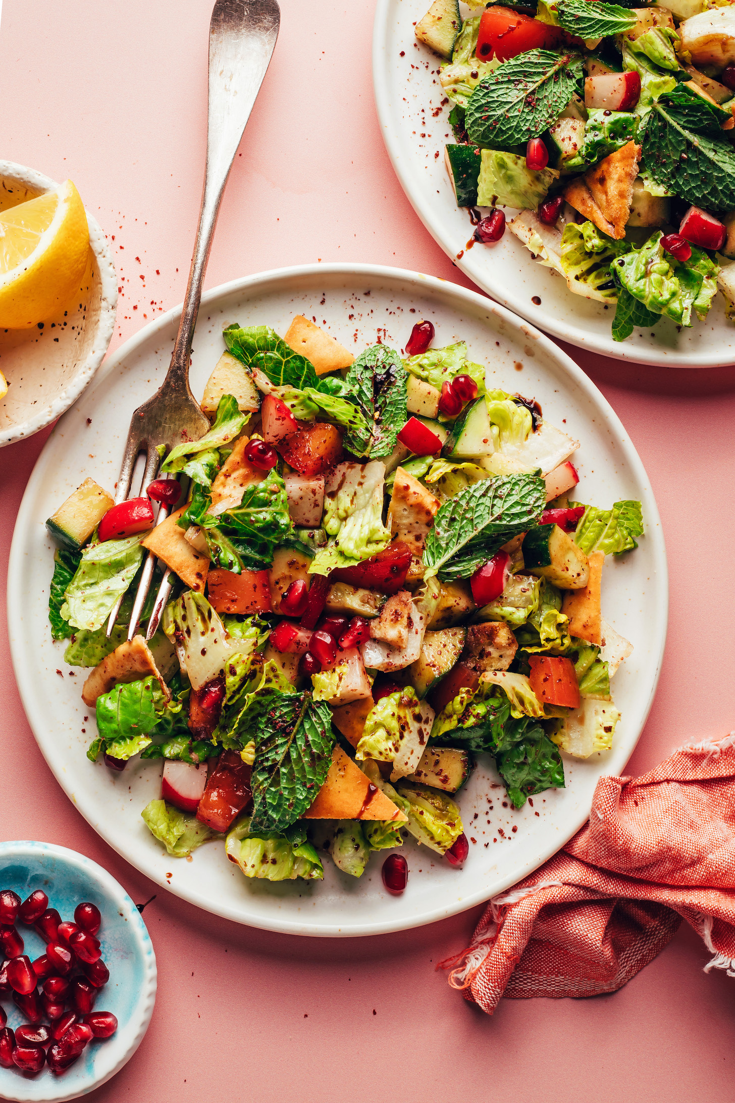 Fattoush salad on serving plates next to pomegranate arils and lemon wedges