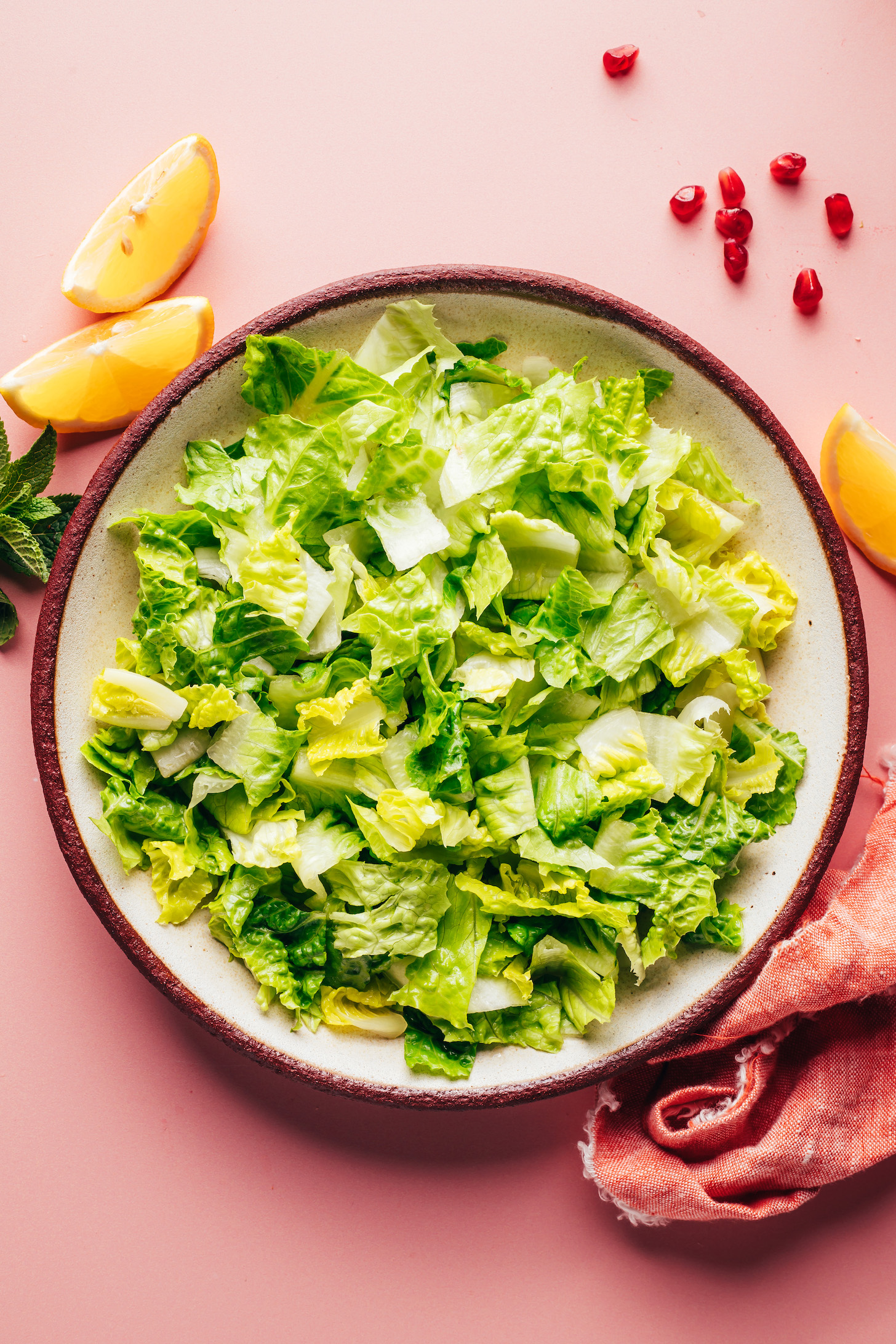 Bowl of chopped romaine lettuce next to fresh mint, lemon wedges, and pomegranate arils