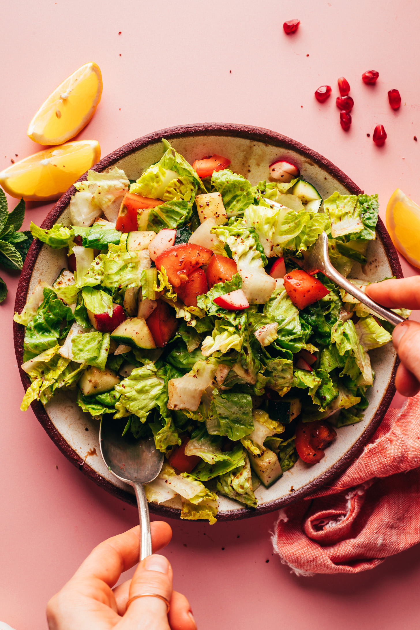 Using a serving spoon and fork to toss the veggies with lemon pomegranate dressing