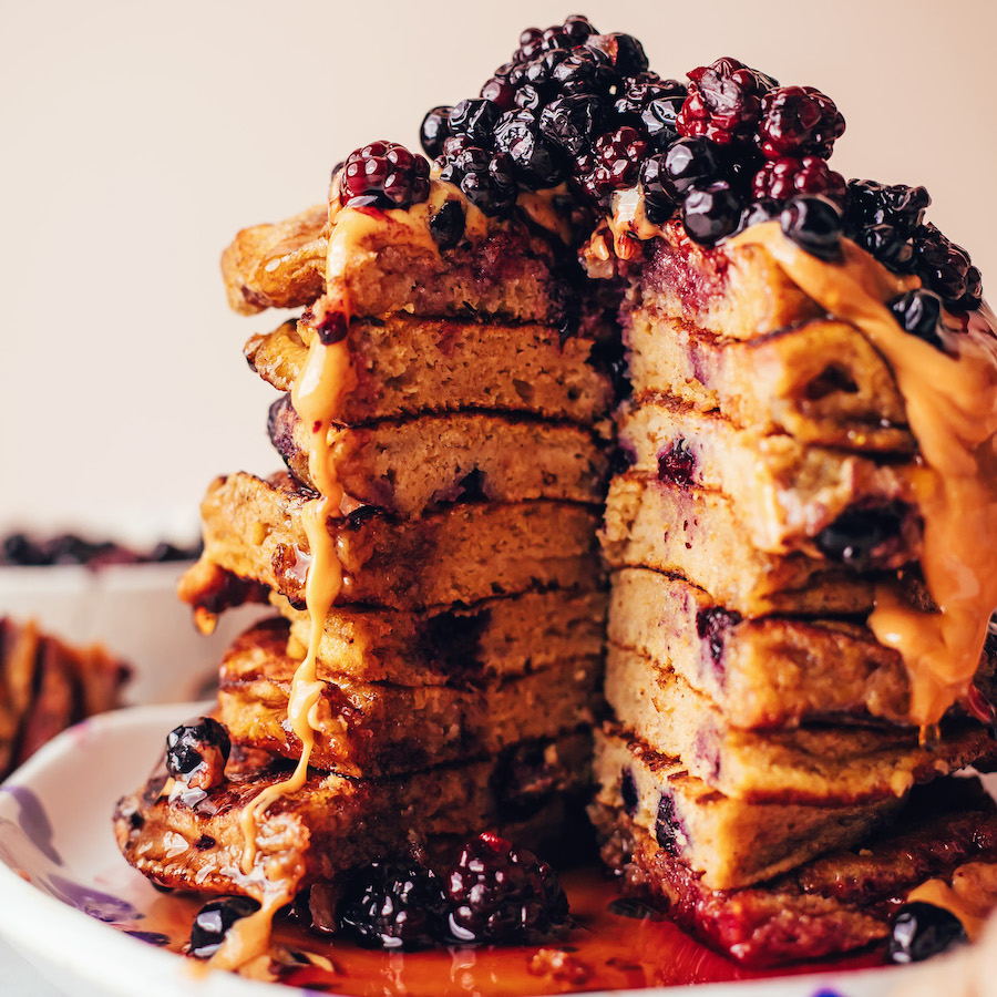 Photo of a tall stack of plantain pancakes with toppings and a slice removed