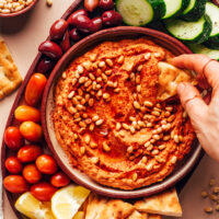 Overhead shot of dipping a slice of pita into a bowl of sun-dried tomato hummus