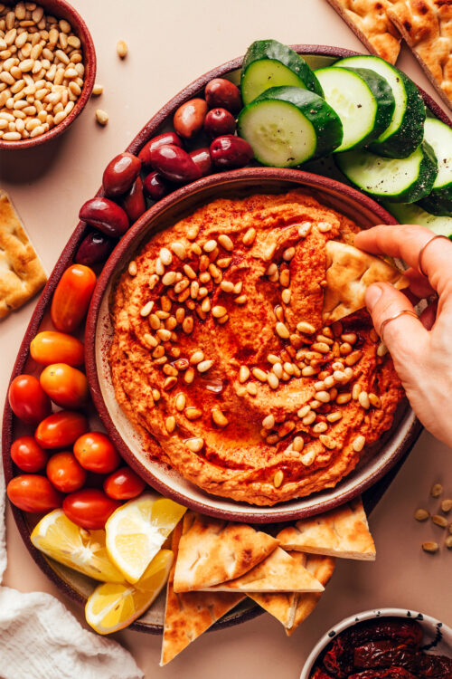Overhead shot of dipping a slice of pita into a bowl of sun-dried tomato hummus