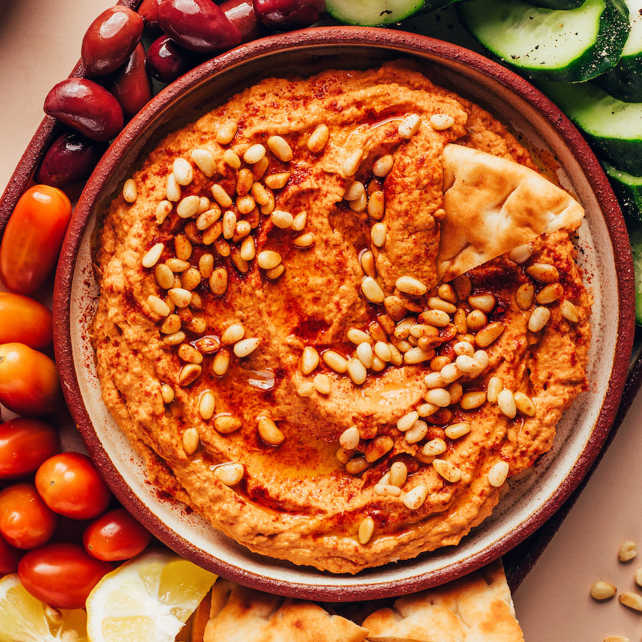 Overhead shot of a bowl of sun-dried tomato hummus on a platter with veggies and pita for dipping
