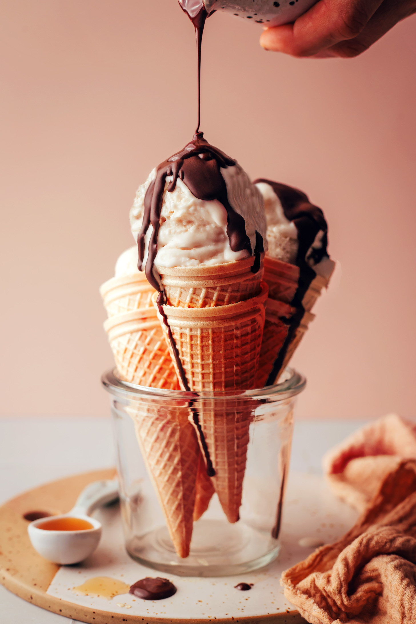 Drizzling chocolate magic shell onto cones with scoops of vegan vanilla soft serve
